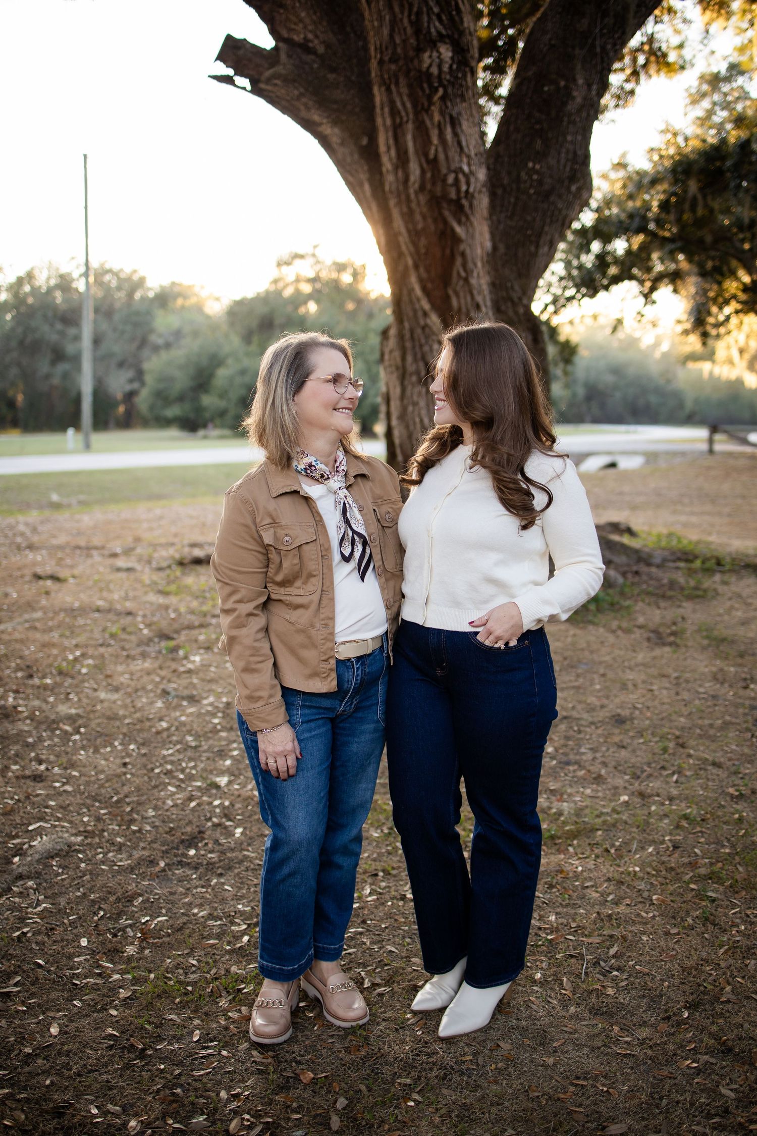 Two people in casual attire share a moment while standing beneath a large tree.