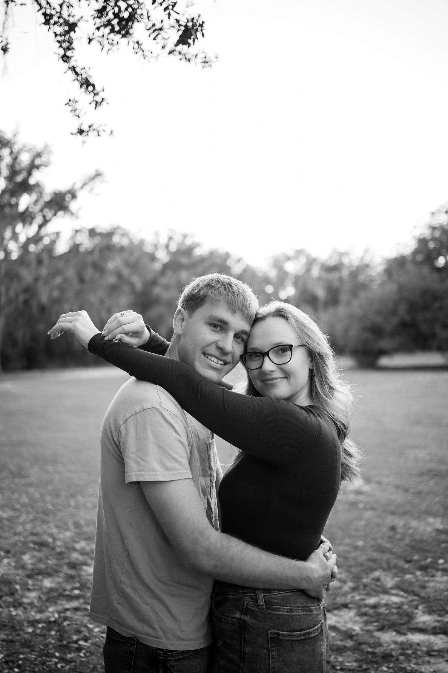 Black and white photo of couple embracing outdoors in a natural setting.