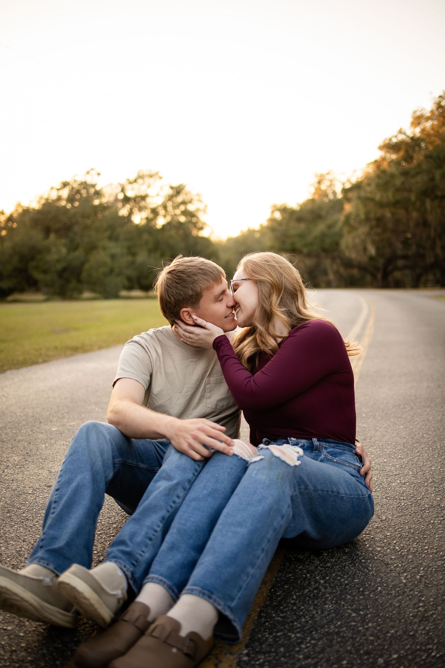 A couple sits together on a road during sunset sharing an intimate moment.