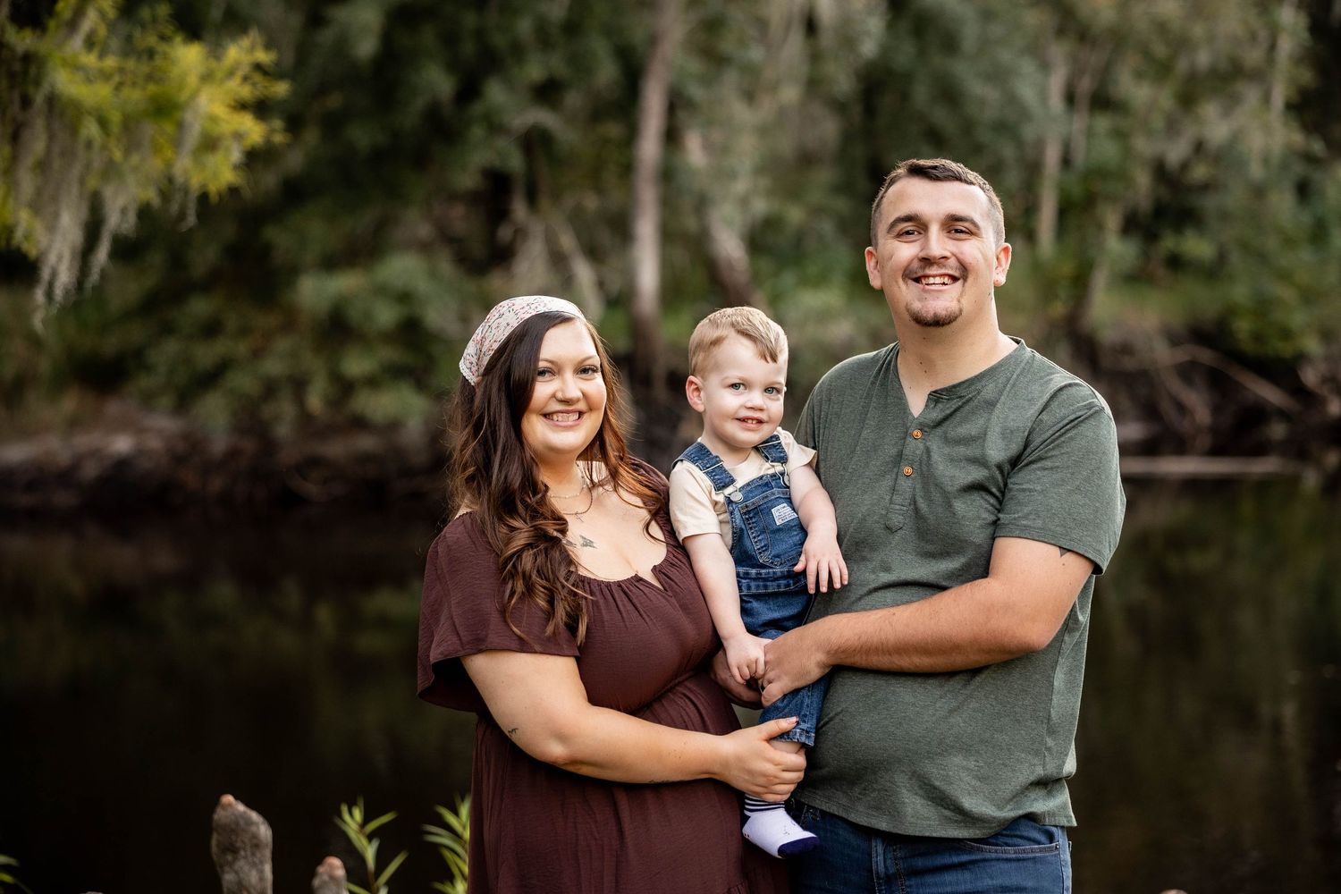 Family poses together outdoors near a lake during autumn photo session.