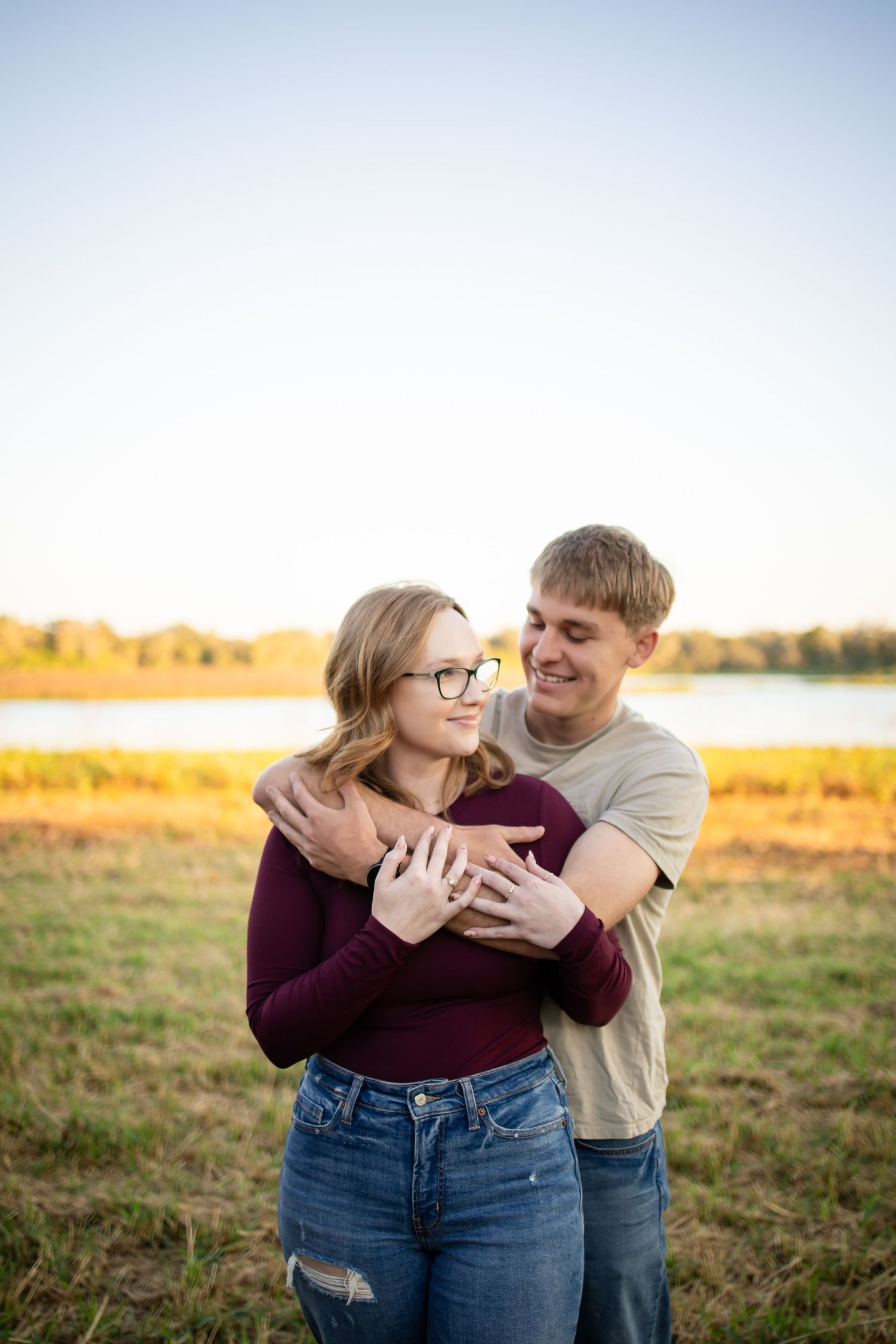 Playful couple laughing together in a sunny field wearing burgundy and beige.