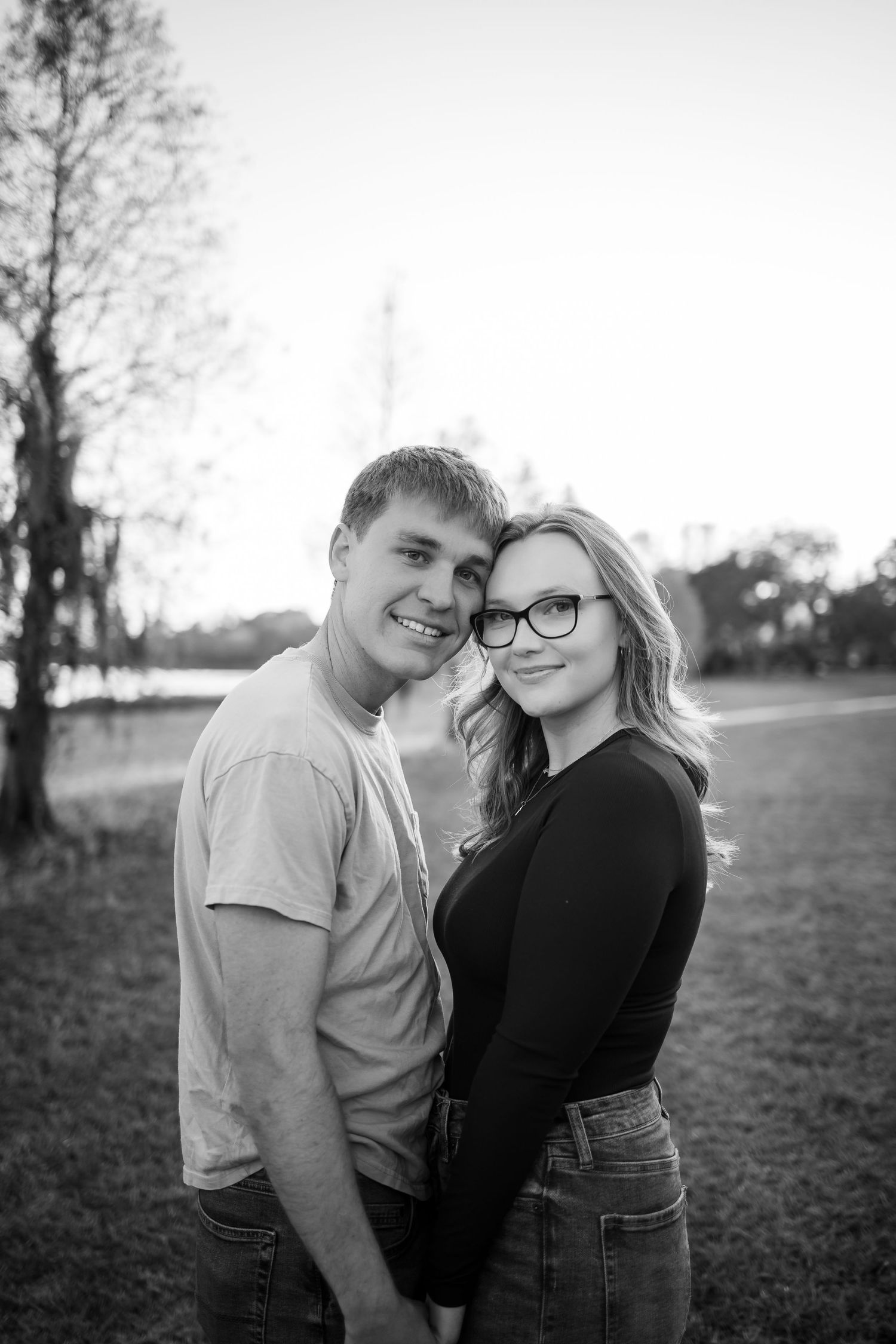 A black and white portrait of a couple laughing together outdoors at sunset.