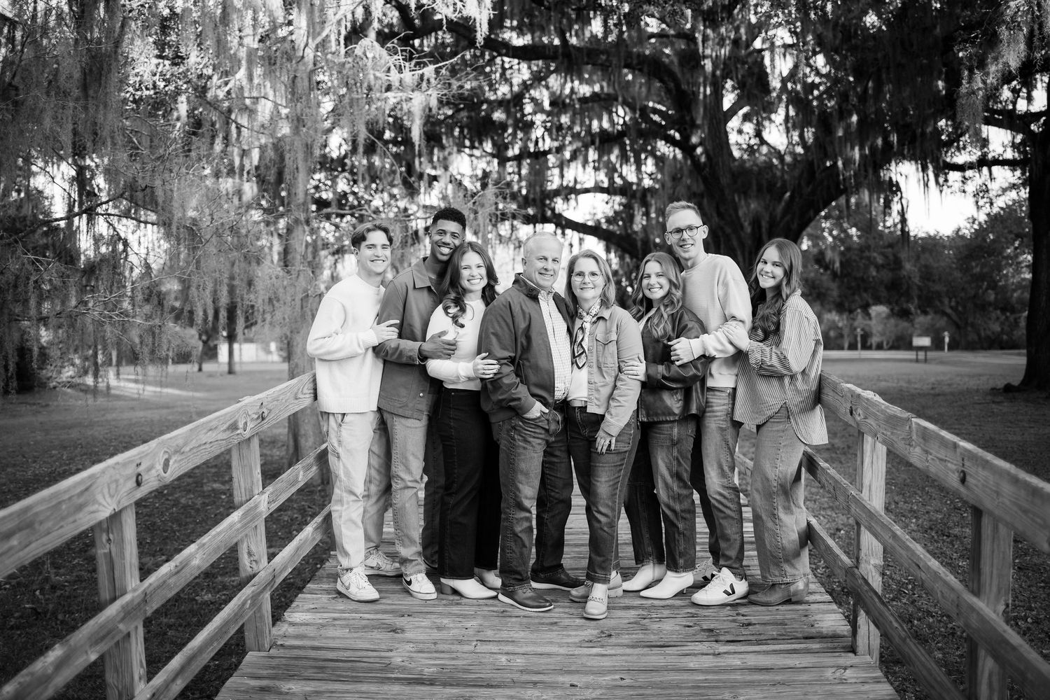 Group portrait of people sitting on wooden fence with Spanish moss draped trees in background.