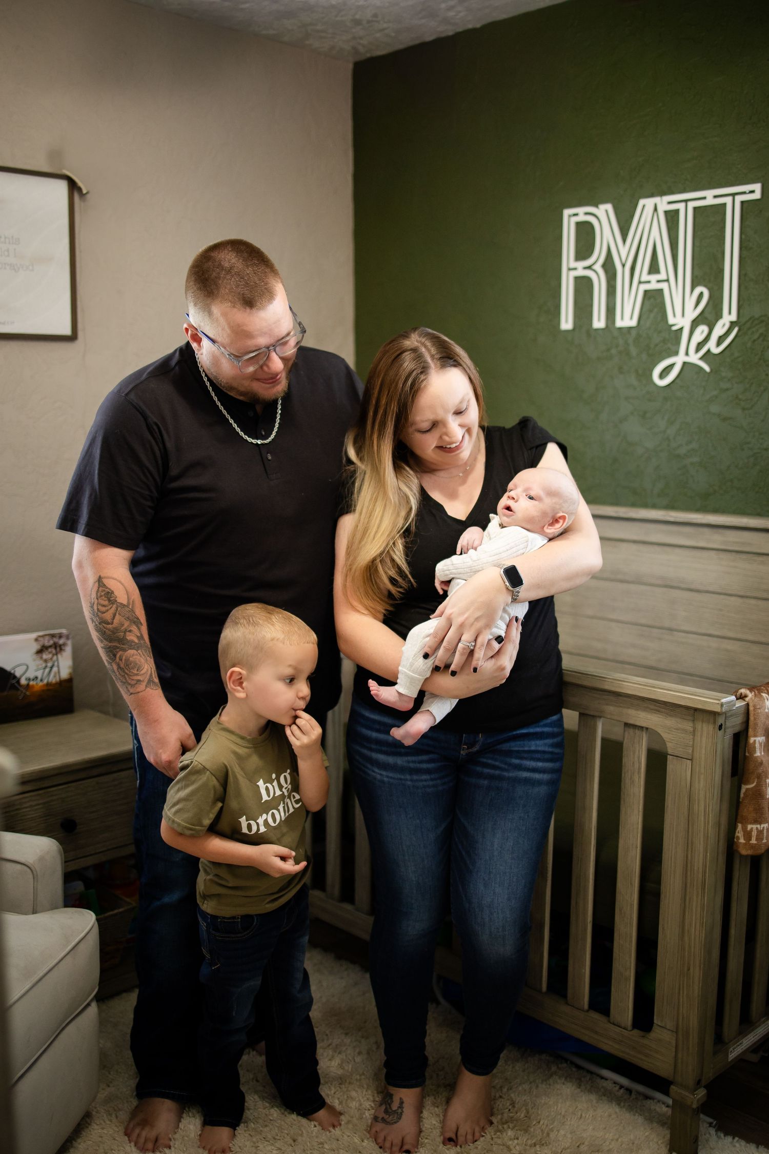 A family poses together in a nursery room with a green accent wall and illuminated neon 