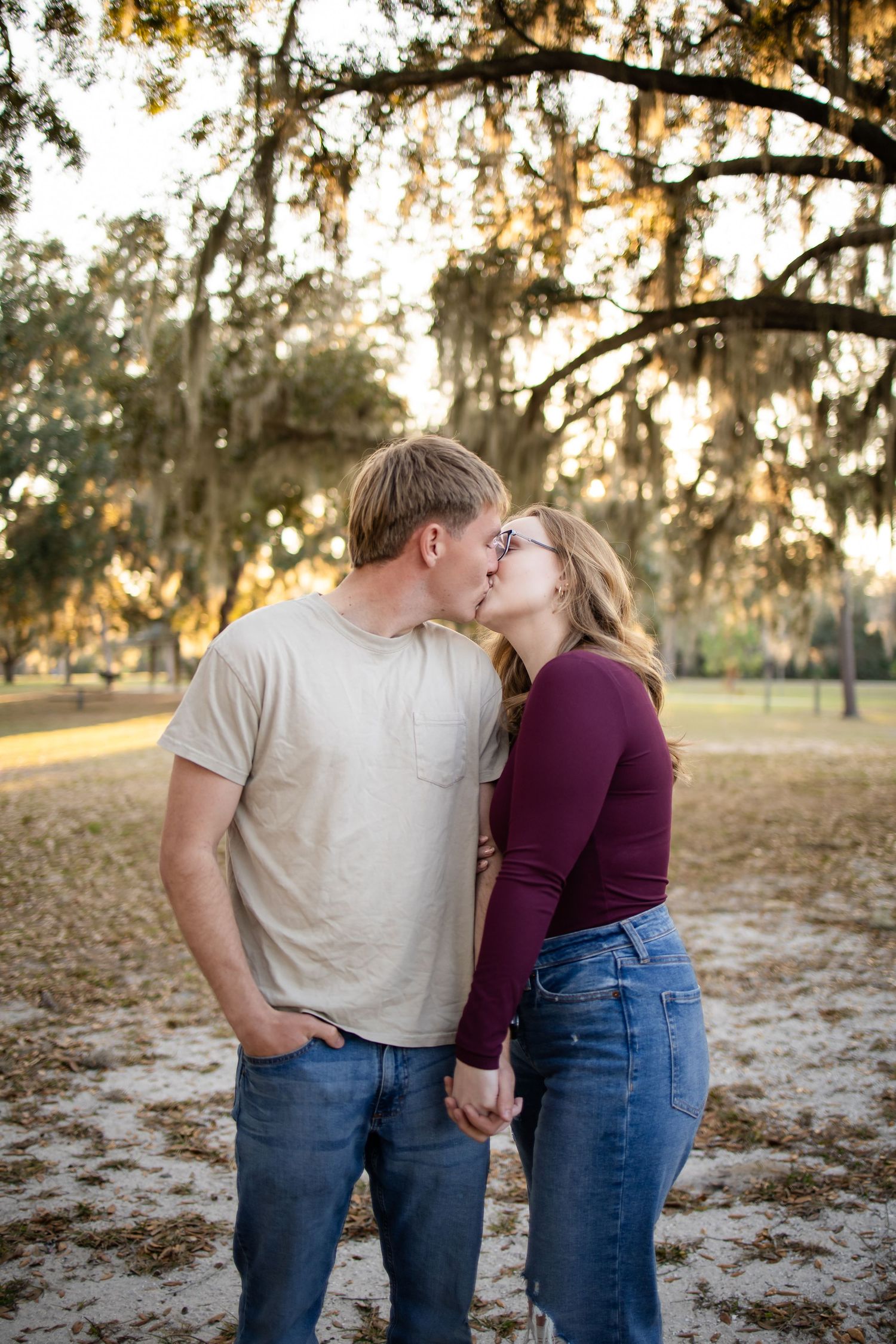 A romantic couple embraces in a park at sunset wearing jeans and casual attire.
