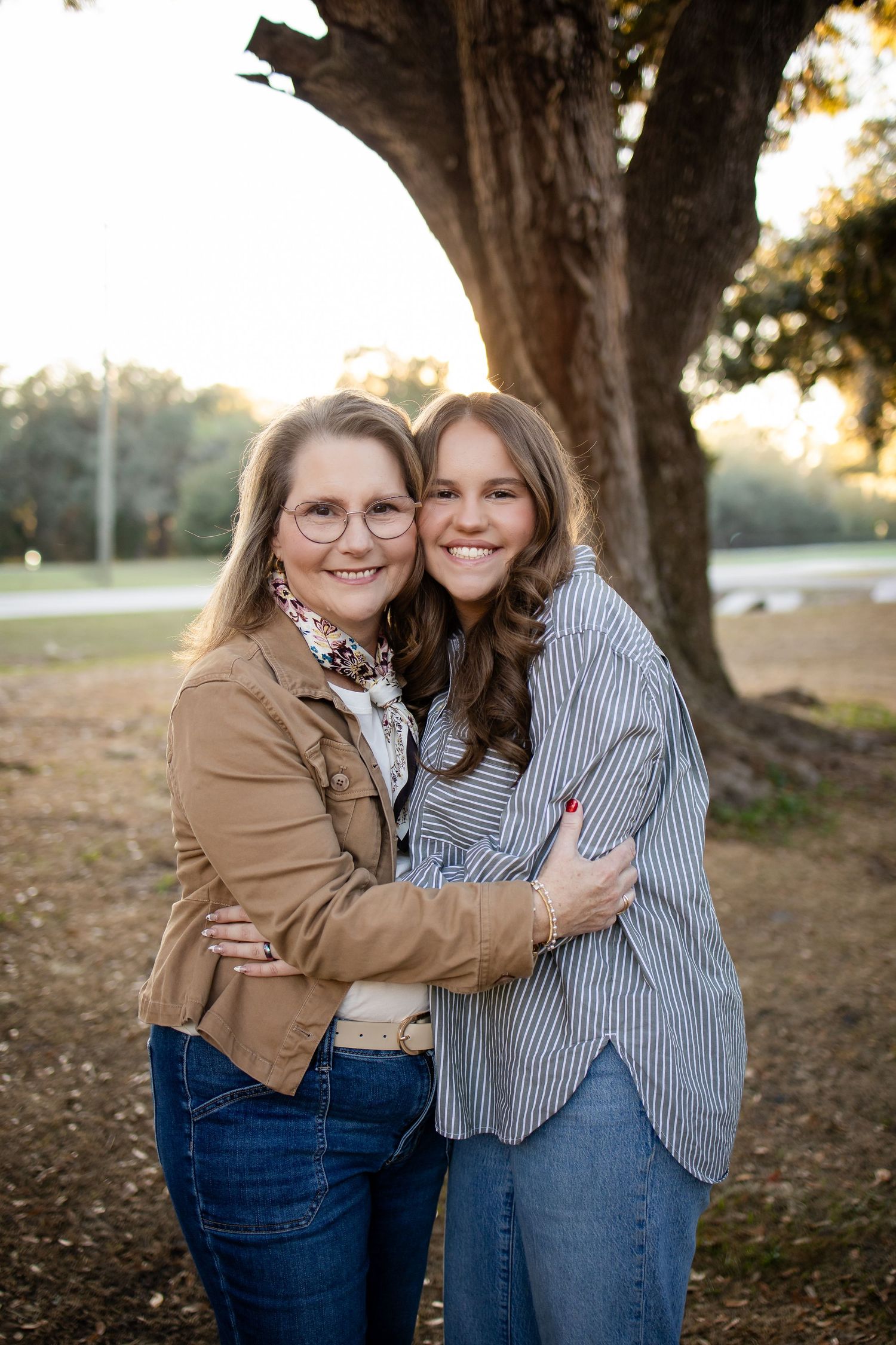 Two people embrace while sharing a warm moment under a large tree.