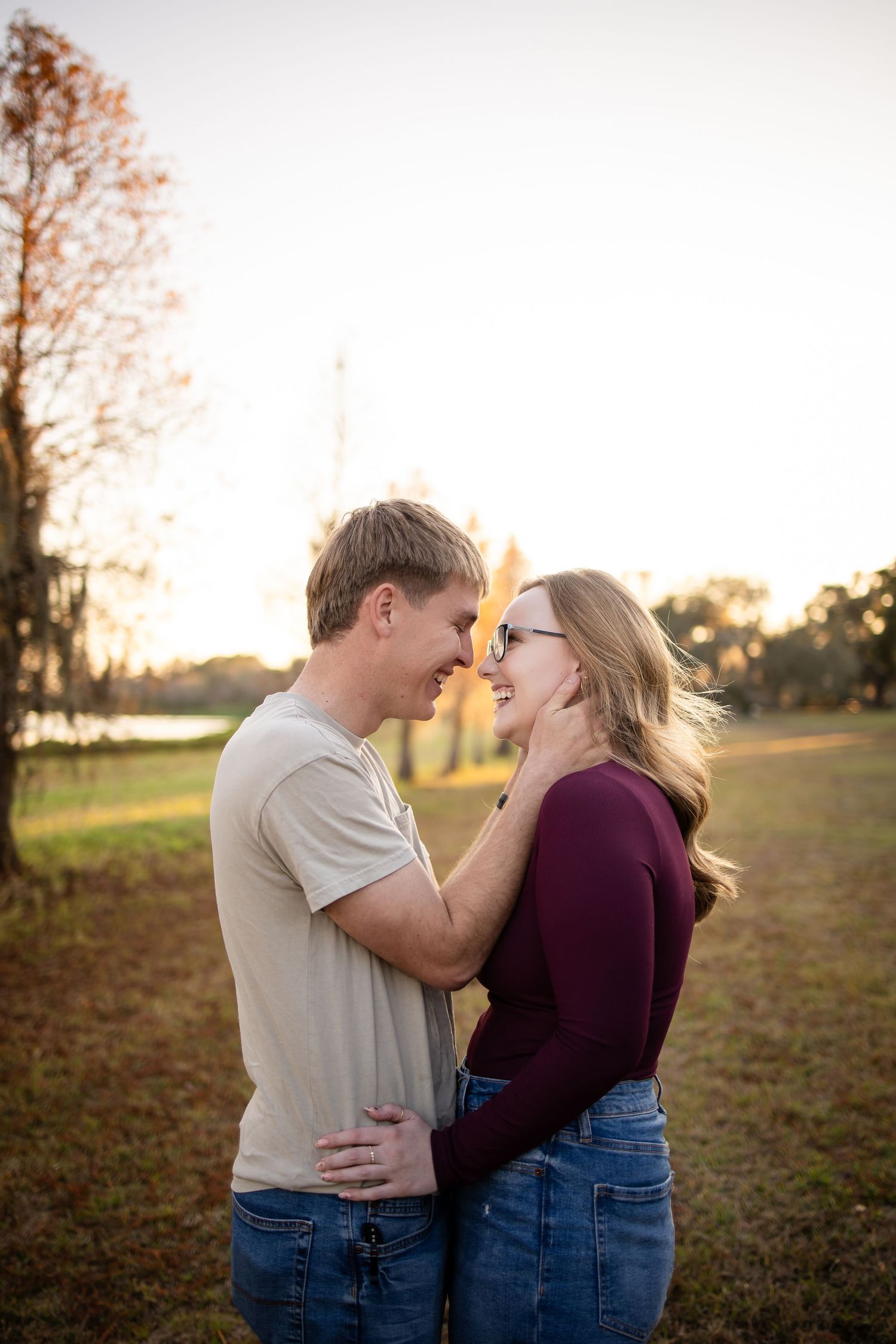 A couple shares an intimate moment at sunset in a park setting with autumn trees in the background.