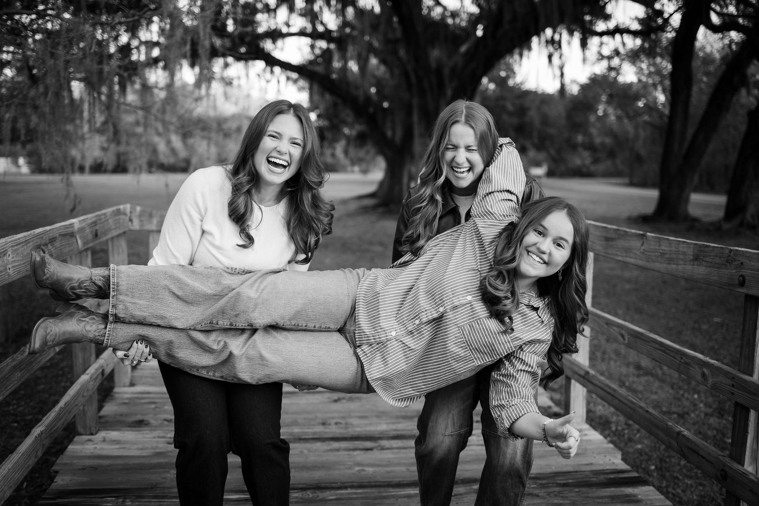 Two people laughing while sitting on wooden fence during outdoor photoshoot.