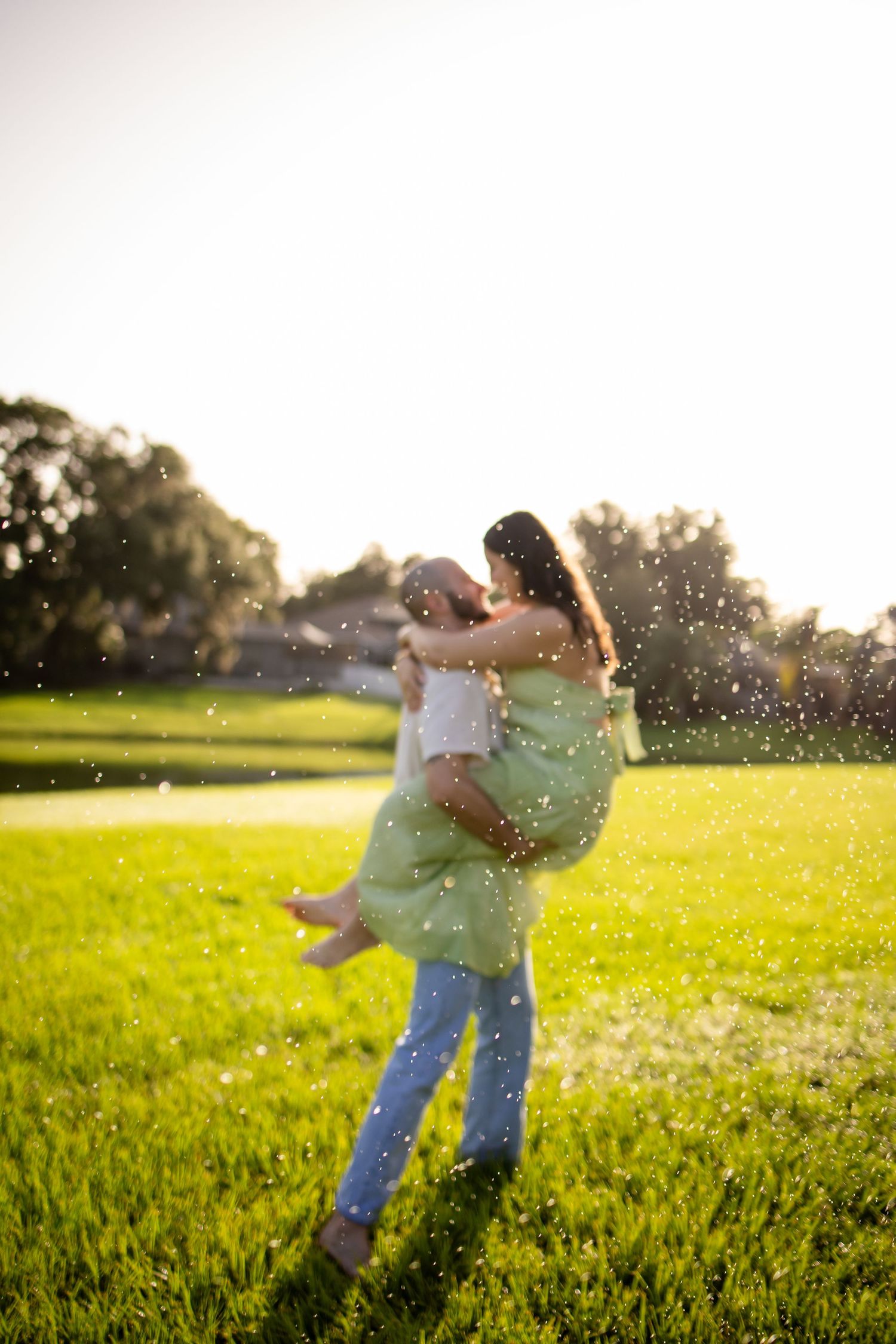Joyful moment captured with water droplets sparkling in sunlight as couple embraces on green lawn.
