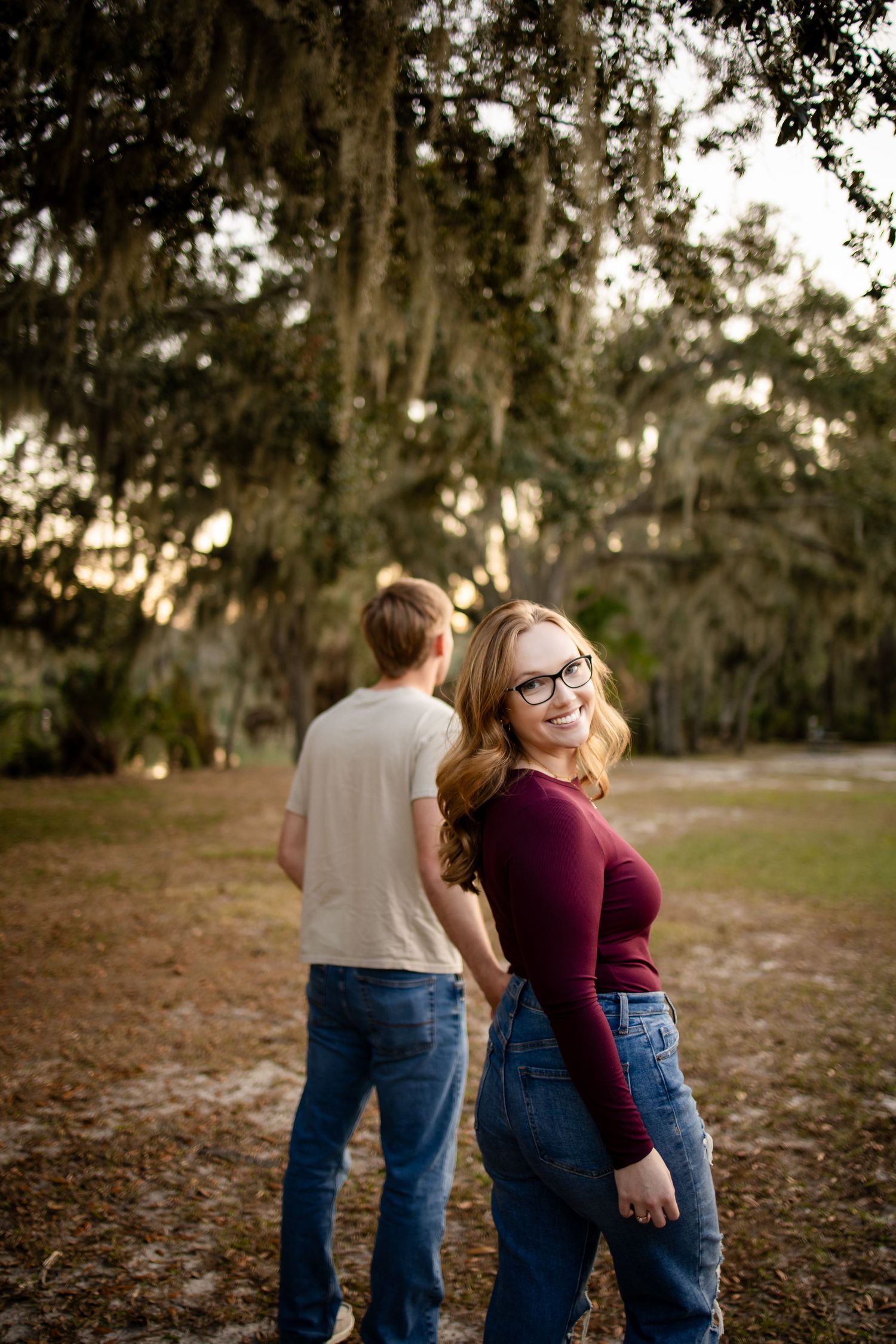 A couple embraces while standing on fallen autumn leaves under Spanish moss draped trees.