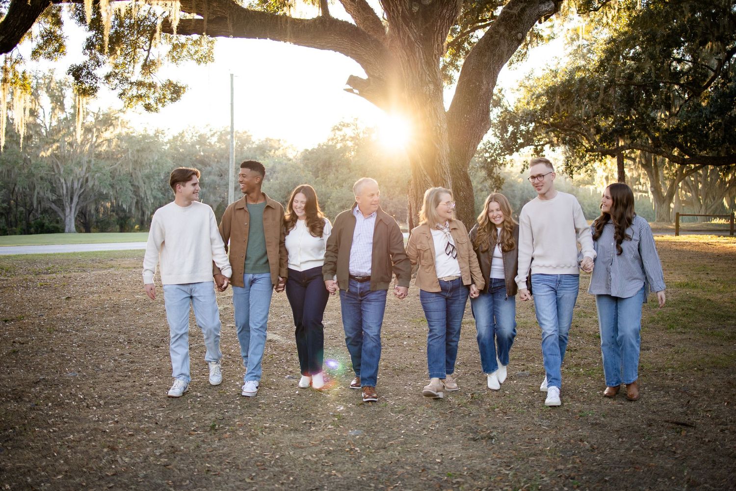 A group walking together in blue jeans along a tree-lined path at sunset.