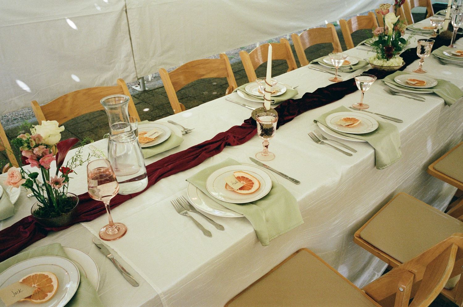 Elegant wedding reception table set with white linens, burgundy runners, candles, floral centerpieces, and formal place settings.