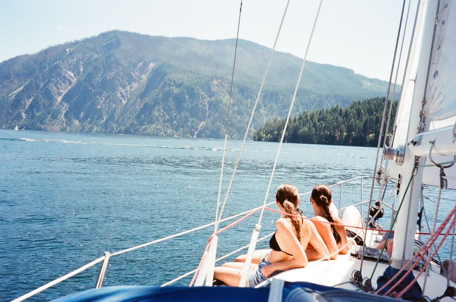 Sailboats cruise along scenic mountain coastline on a sunny summer day.