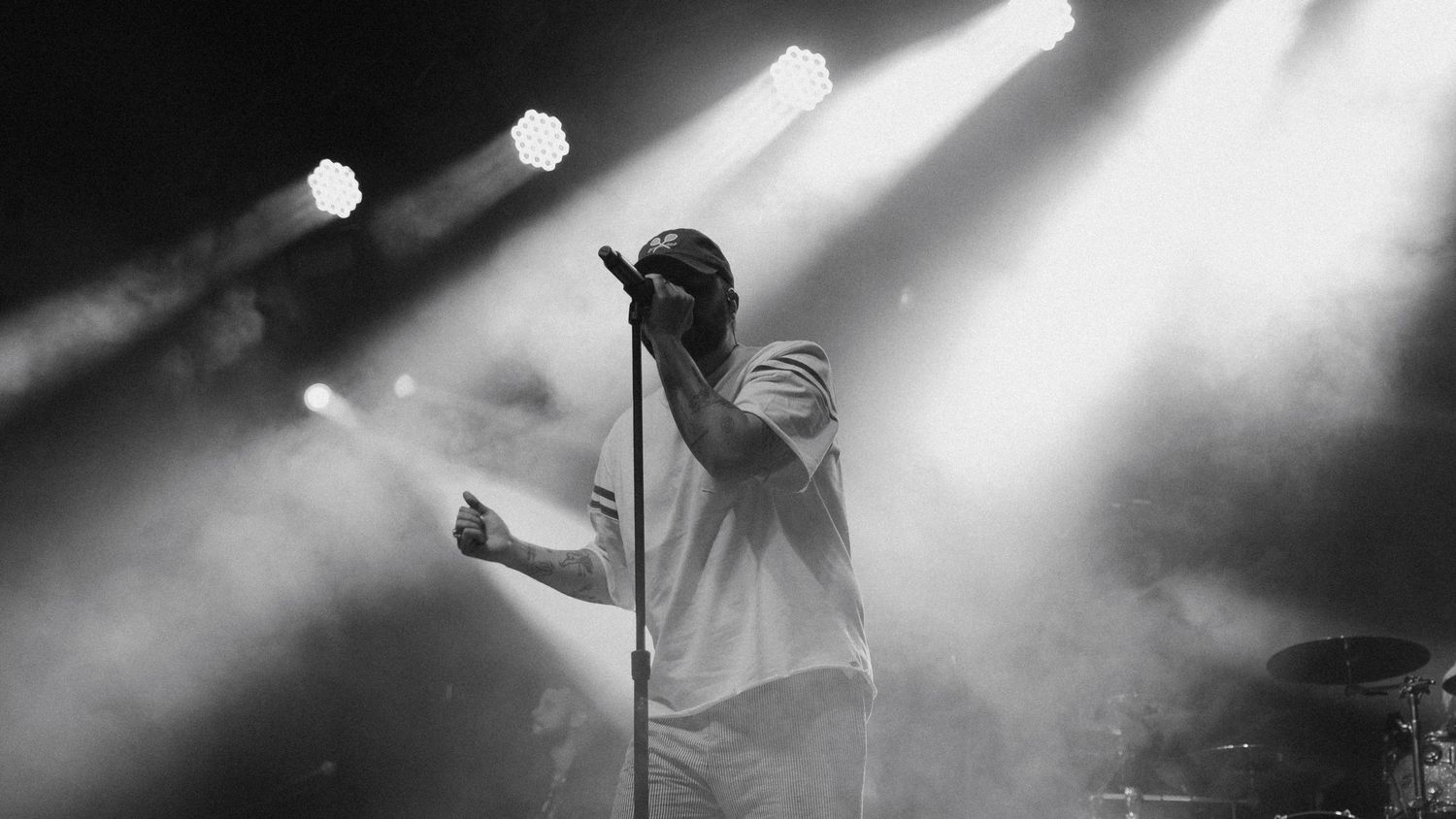 Performer on stage illuminated by dramatic spotlights during concert performance.