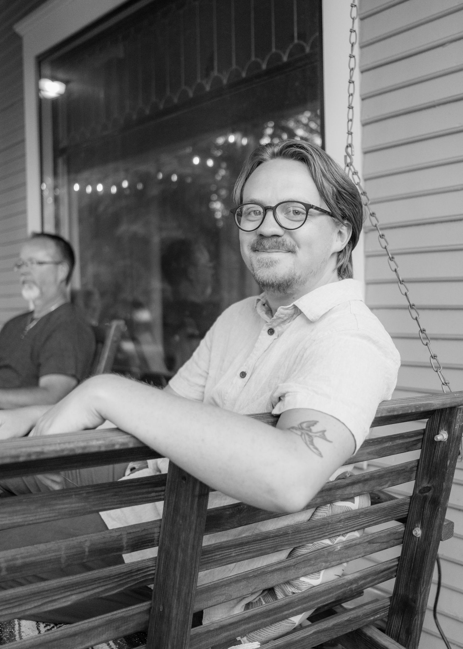 Person relaxing on wooden porch swing with string lights in background.