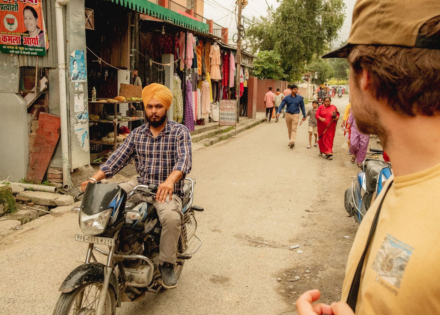 Street scene in Nepal with motorcyclist and pedestrians walking past colorful storefronts.