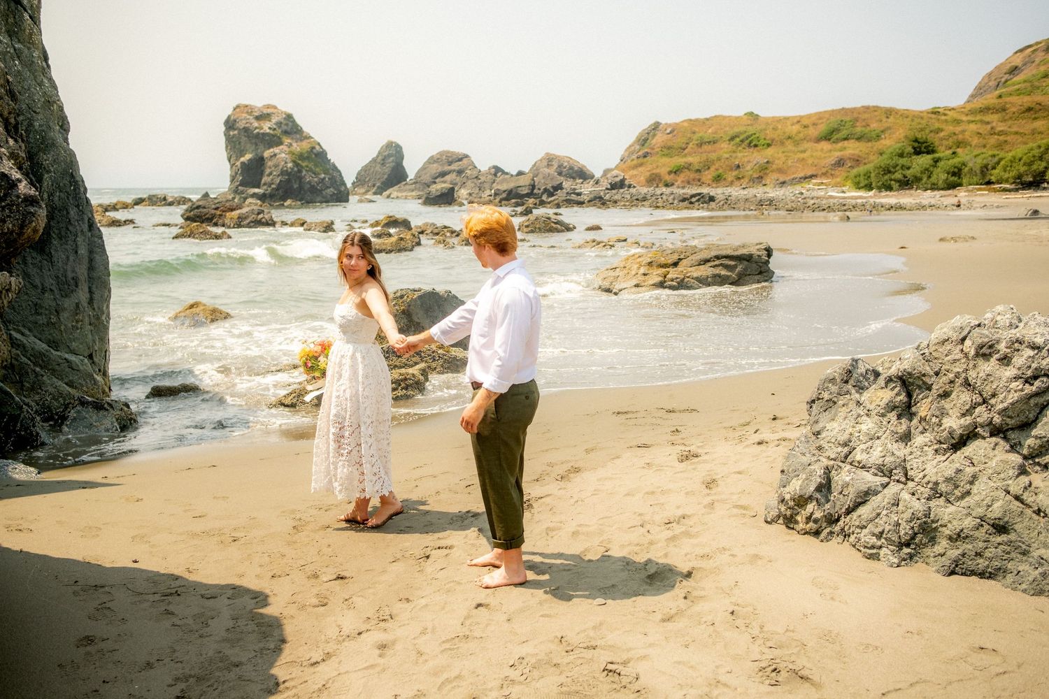 Couple sharing a romantic moment on a beach with dramatic rock formations in the background.