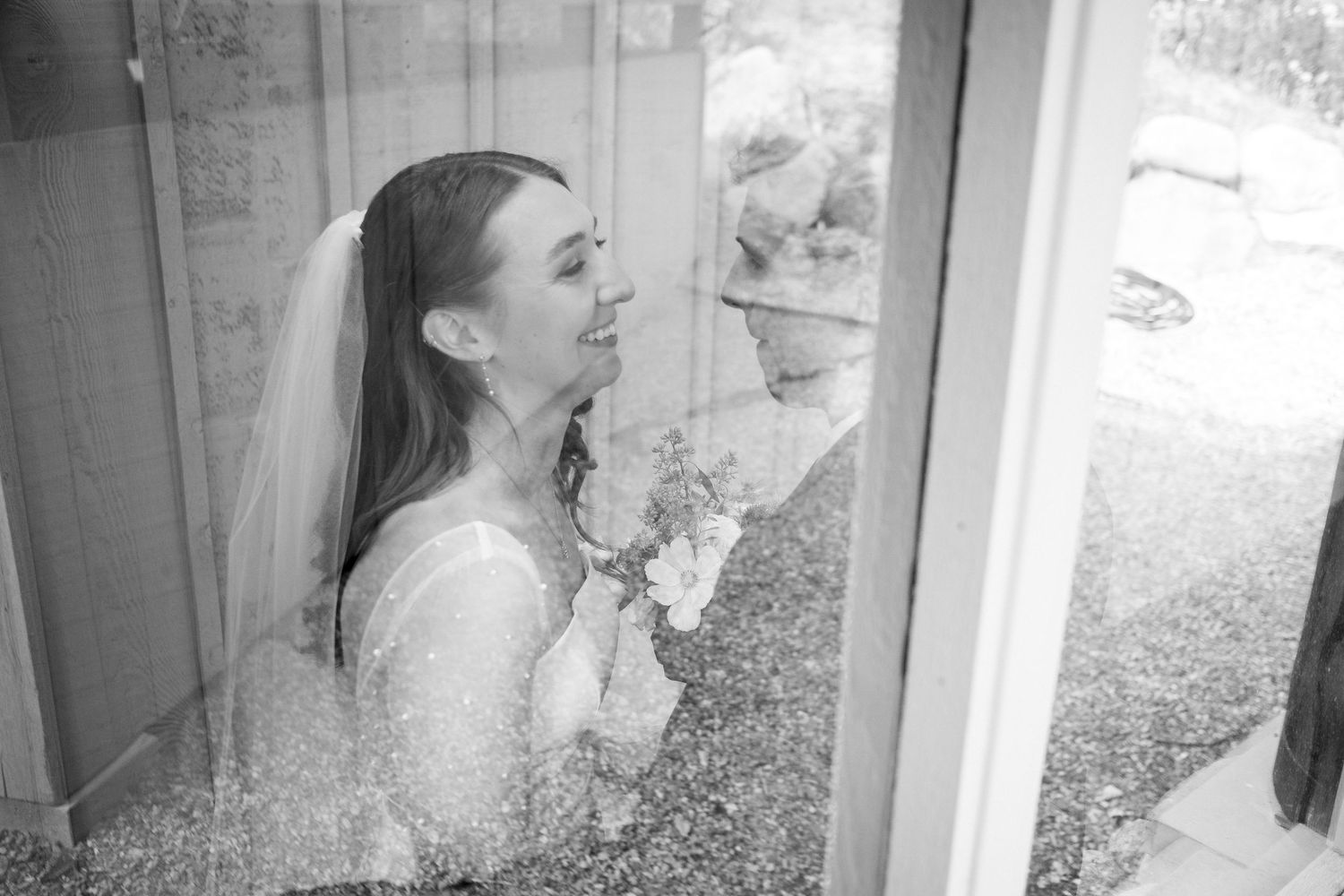 Black and white photo of someone in a wedding dress looking through a window.