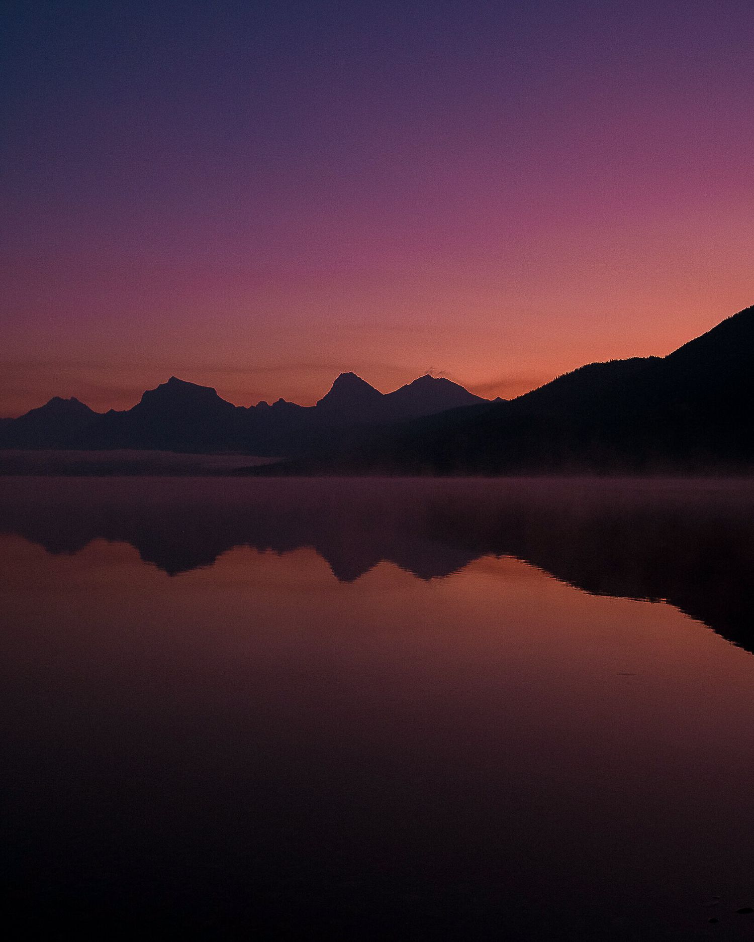 Purple and pink sunset over mountain lake with perfect reflection on calm water.