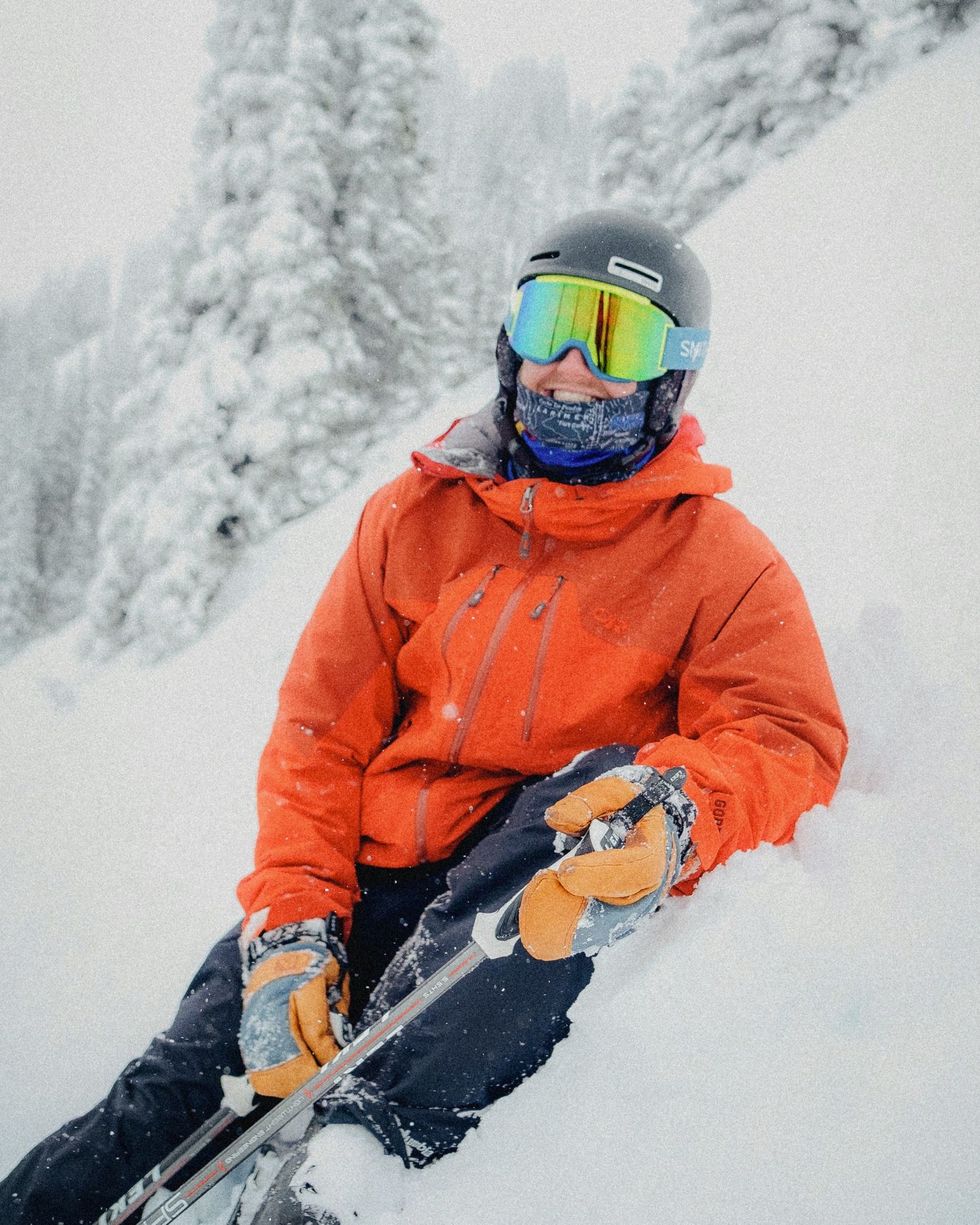 Skier in bright orange jacket and reflective goggles navigating snowy slopes on a foggy winter day.