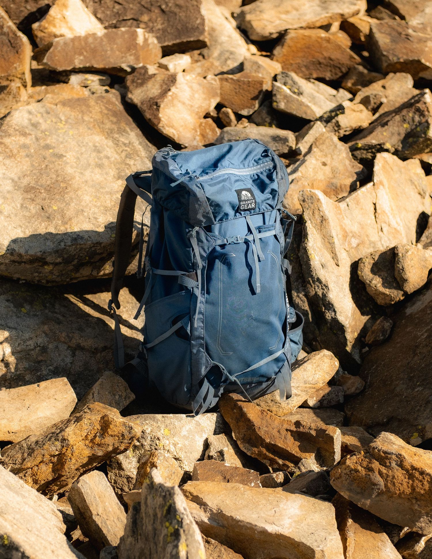 Blue hiking backpack placed on rocky terrain in warm sunlight.