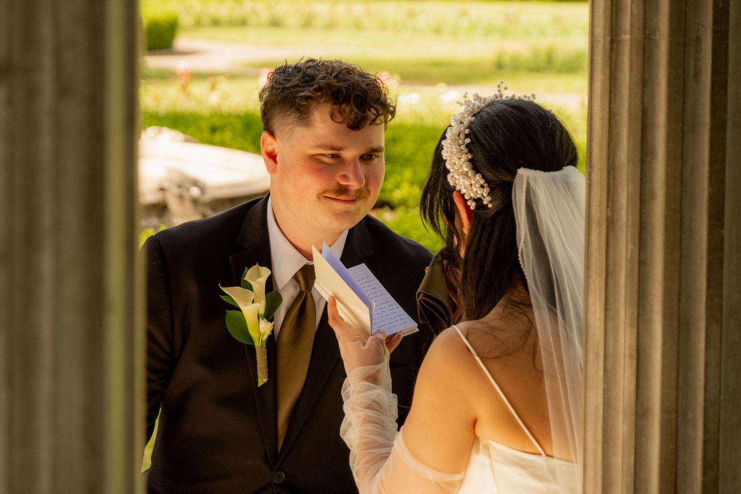 Bride in white veil adjusts groom's tie during outdoor wedding ceremony at elegant venue.