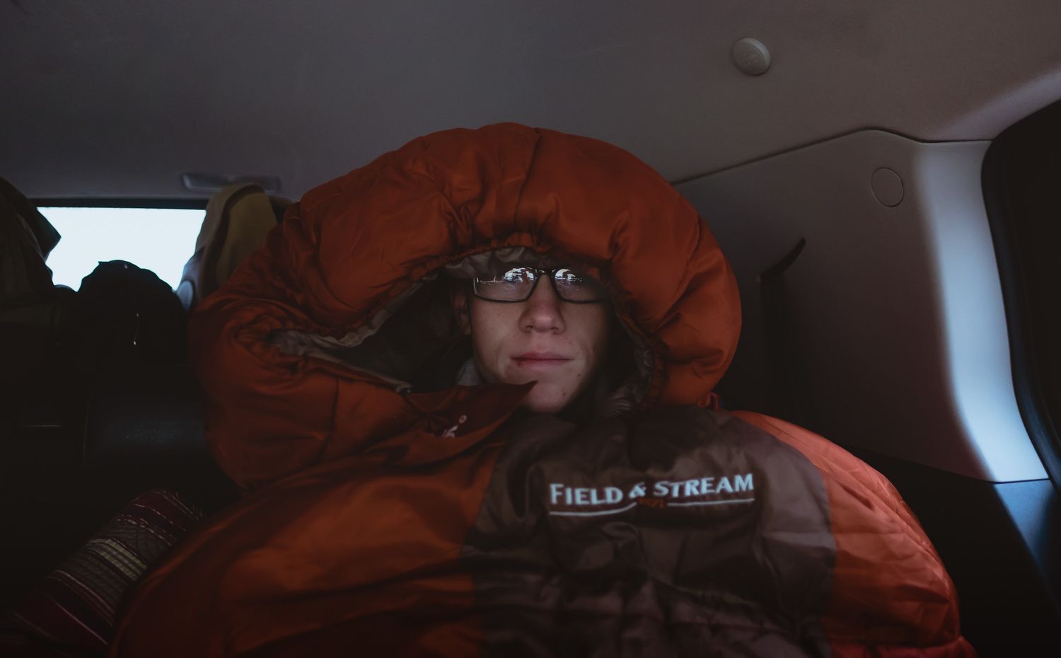 Someone bundled up in a bright orange winter coat rests in a car interior.