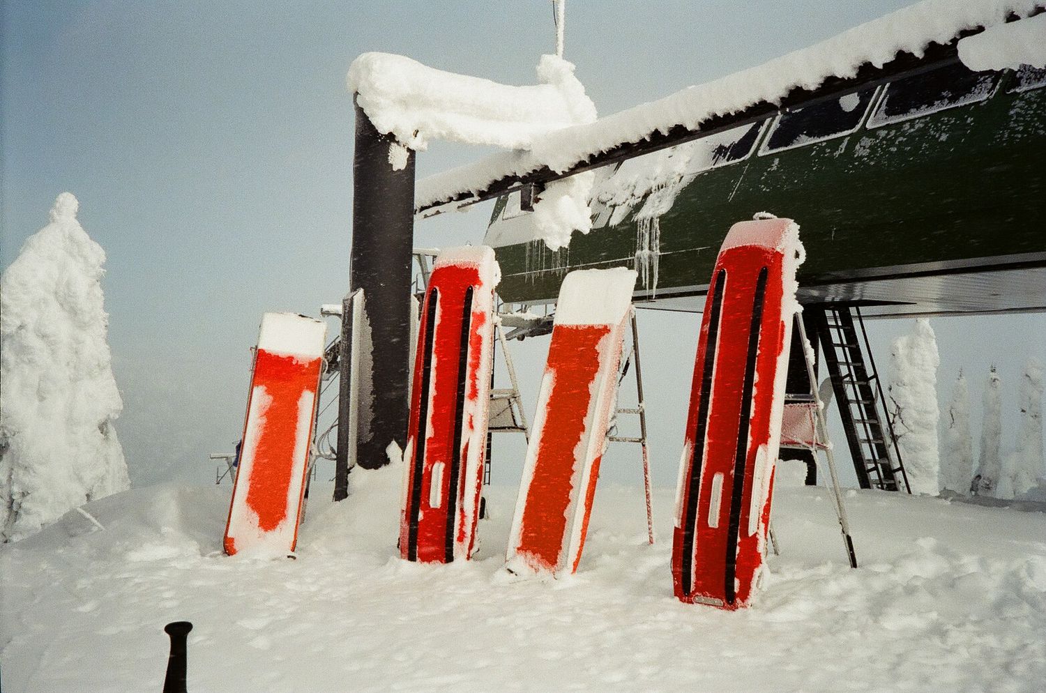 Snow-covered ski lift equipment stands against a winter landscape with heavy frost accumulation.