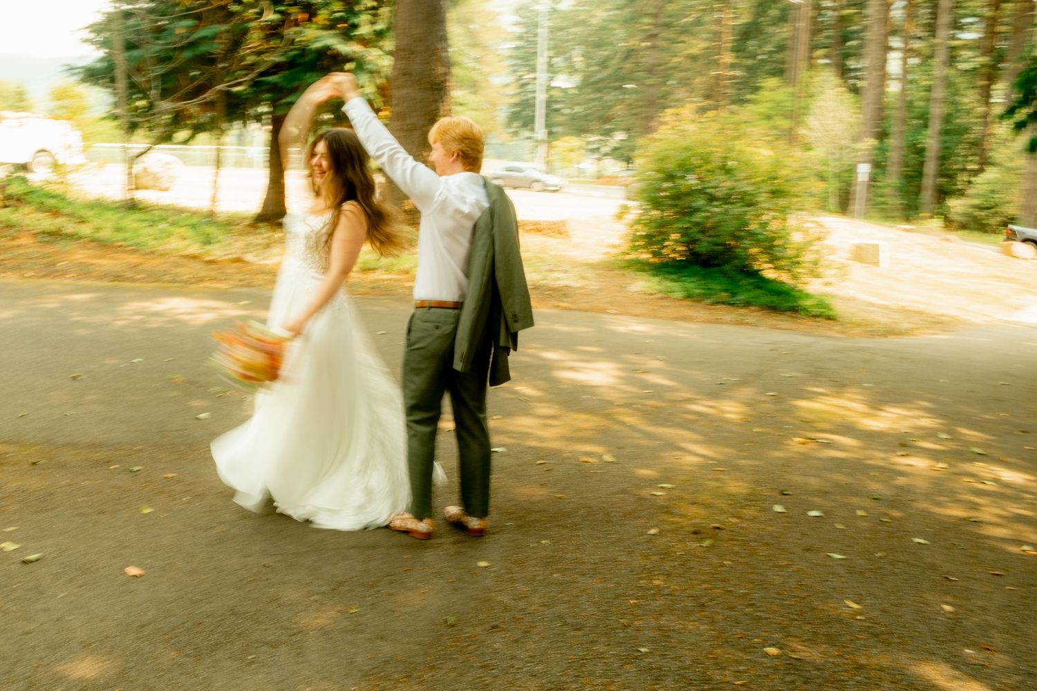 A dreamy wedding couple dancing together on a sunlit forest path.