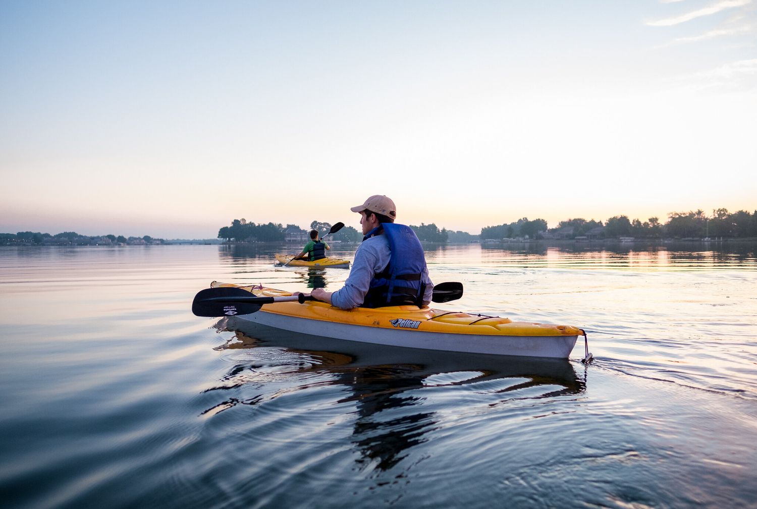 A person kayaking on calm waters during sunrise with a yellow kayak creating ripples in the reflective surface.