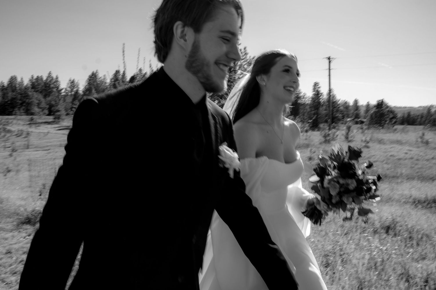 Black and white wedding photo with couple walking through a scenic mountain meadow.
