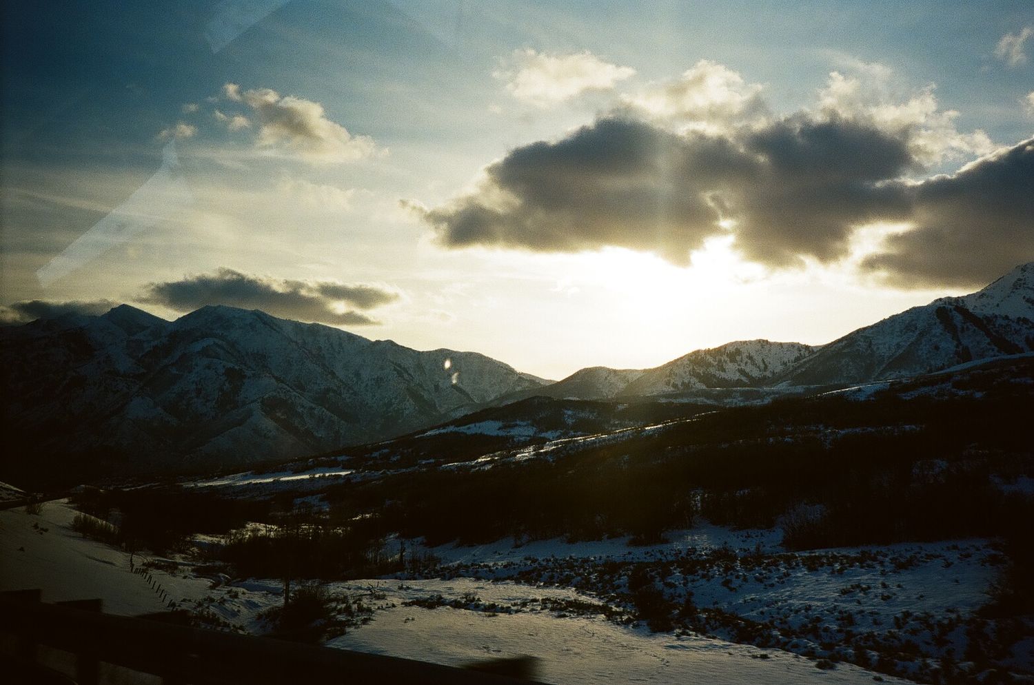 Dramatic sunset over snow-covered mountains with dark clouds silhouetted against the golden sky.