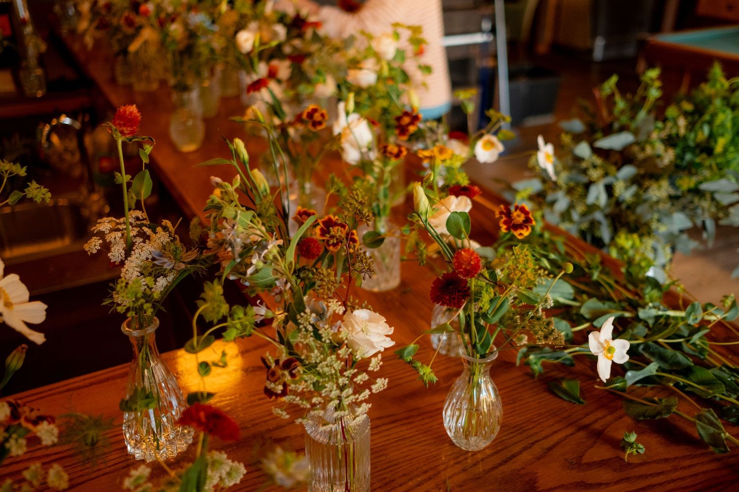 Romantic floral arrangement with wildflowers in glass vases on a wooden table with warm lighting.