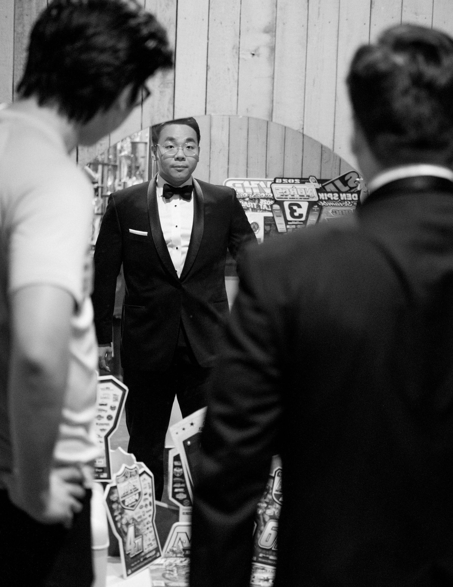 Three men in formal attire, including one in a tuxedo with bow tie, socializing at an elegant black and white event.