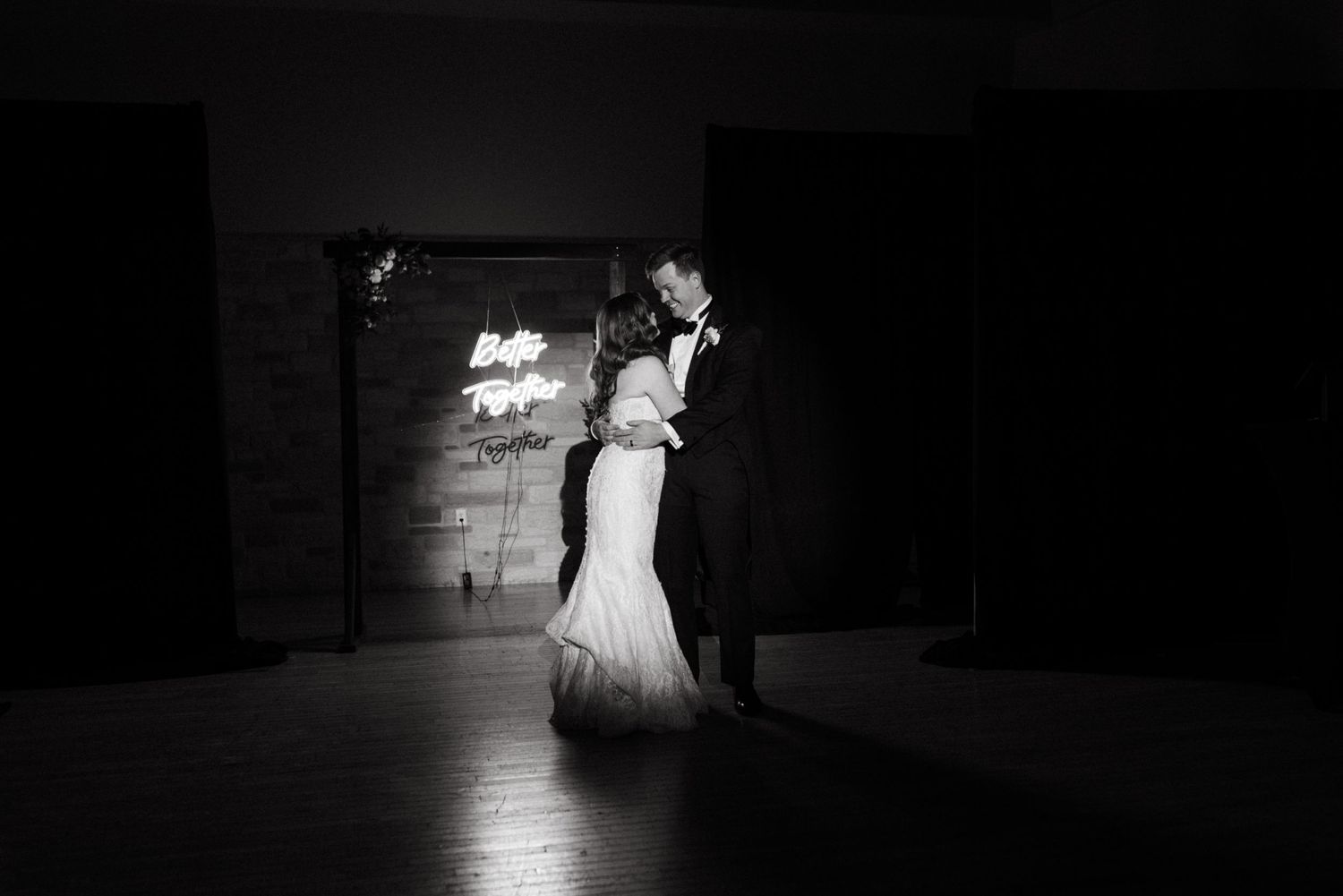 A couple shares their first dance in dramatic lighting under a spotlight.
