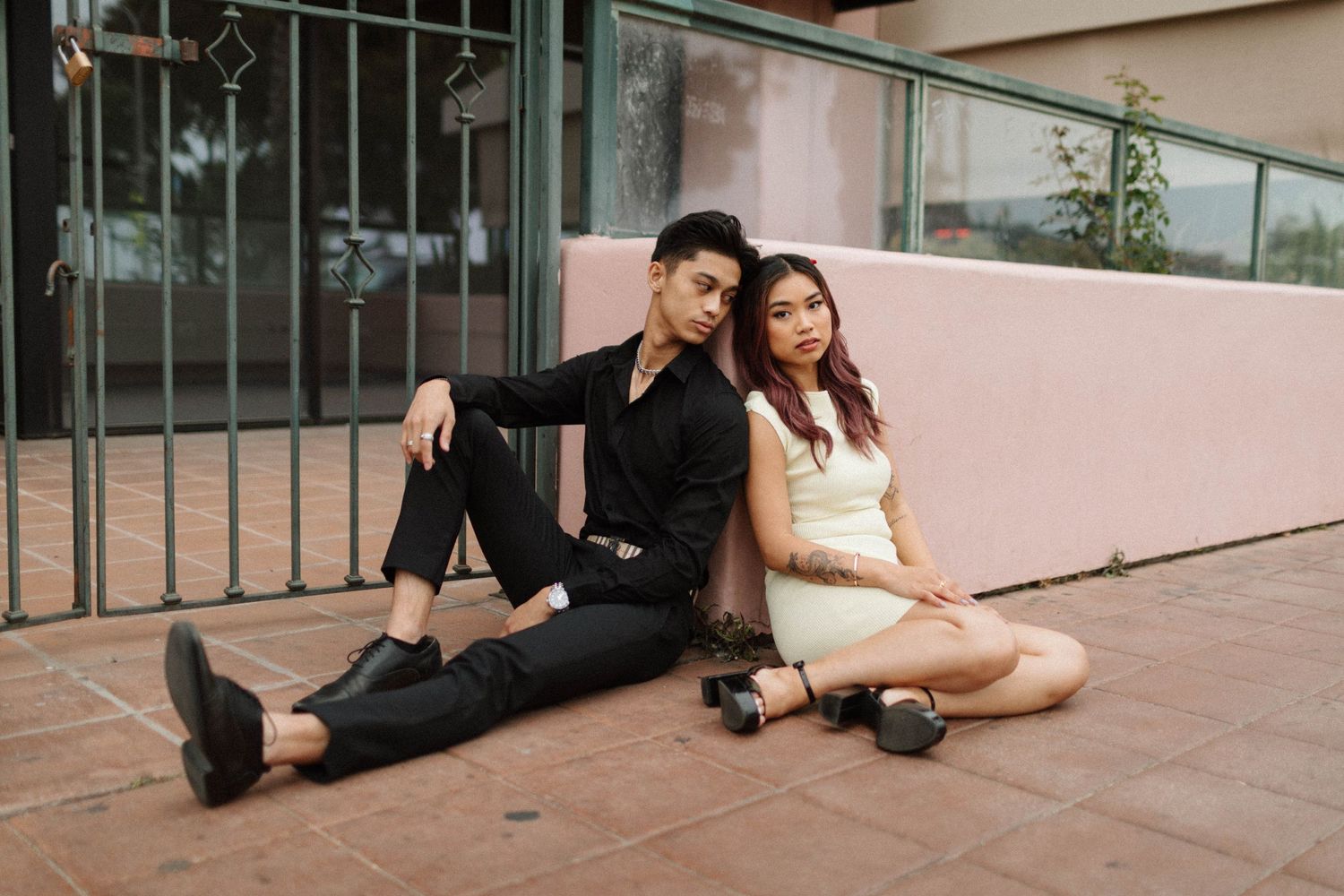 Stylish couple sitting together on pink terrace floor.