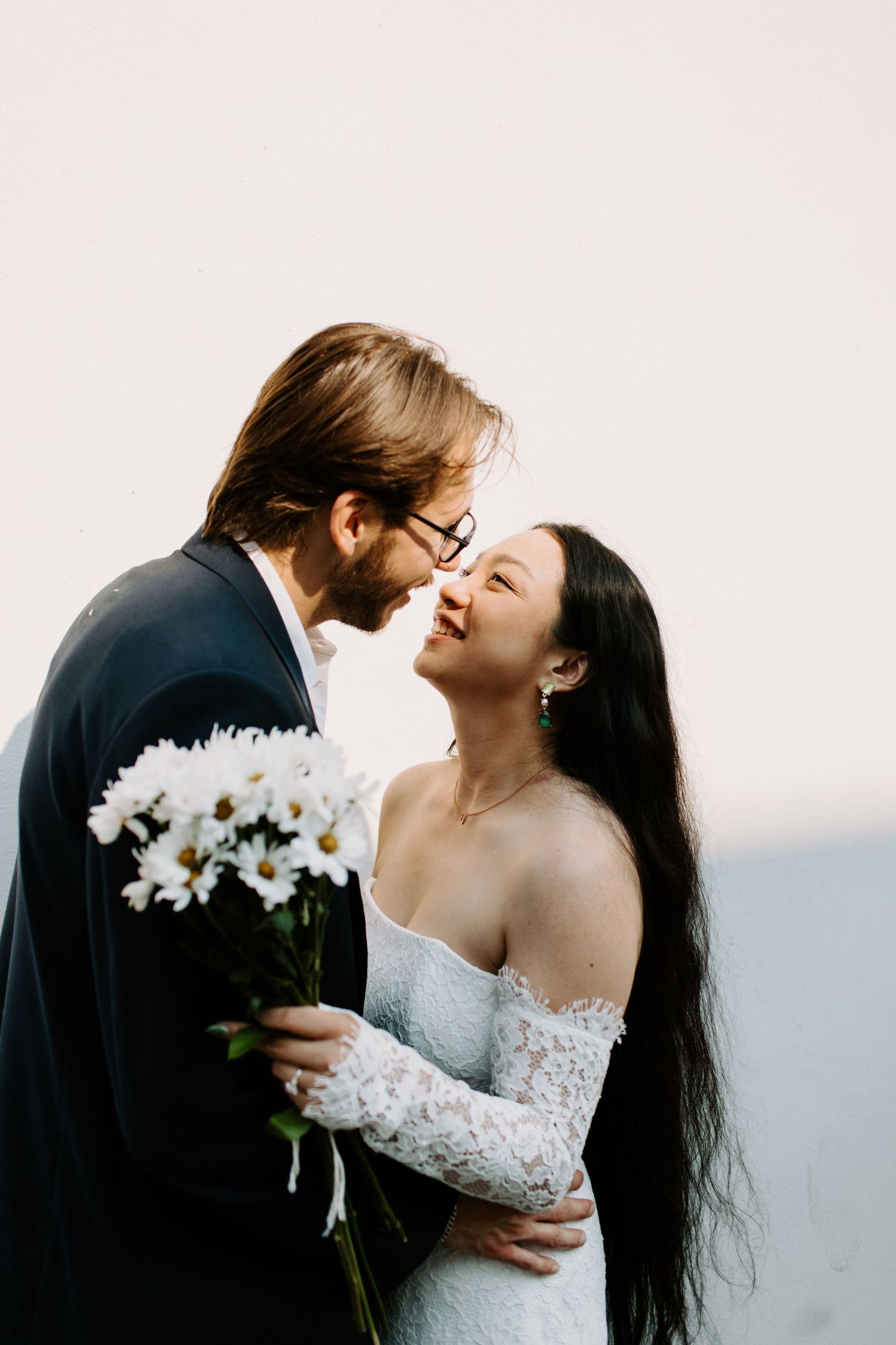 A romantic couple embraces outdoors while holding a bouquet of white daisies and sharing an intimate moment at Waterloo Civil Wedding
