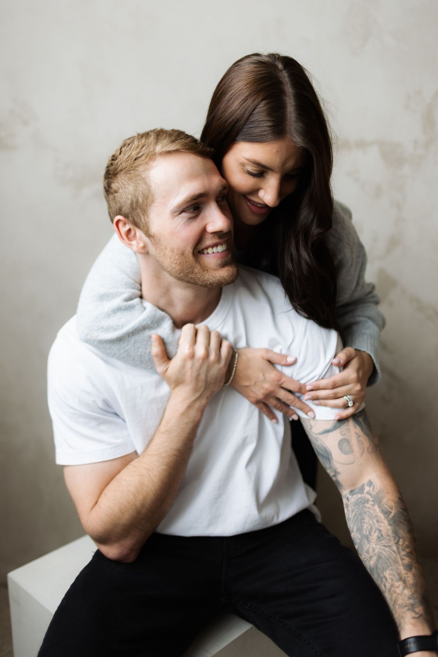 A couple shares an intimate moment hugging and smiling against a neutral background in Toronto Ontario Photo Studio by Alexis Mimacho