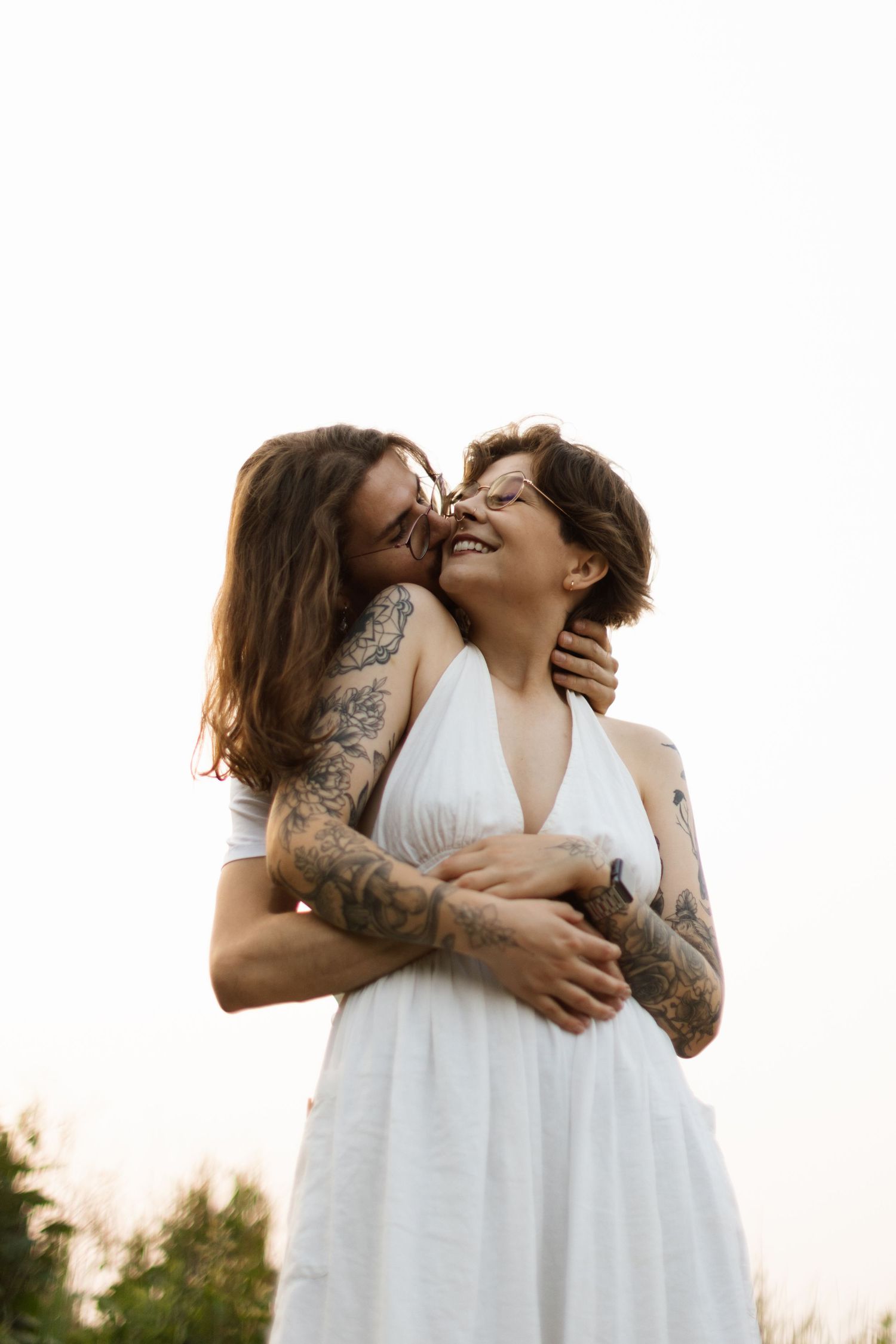 An intimate moment between two people in white dresses against a bright background.