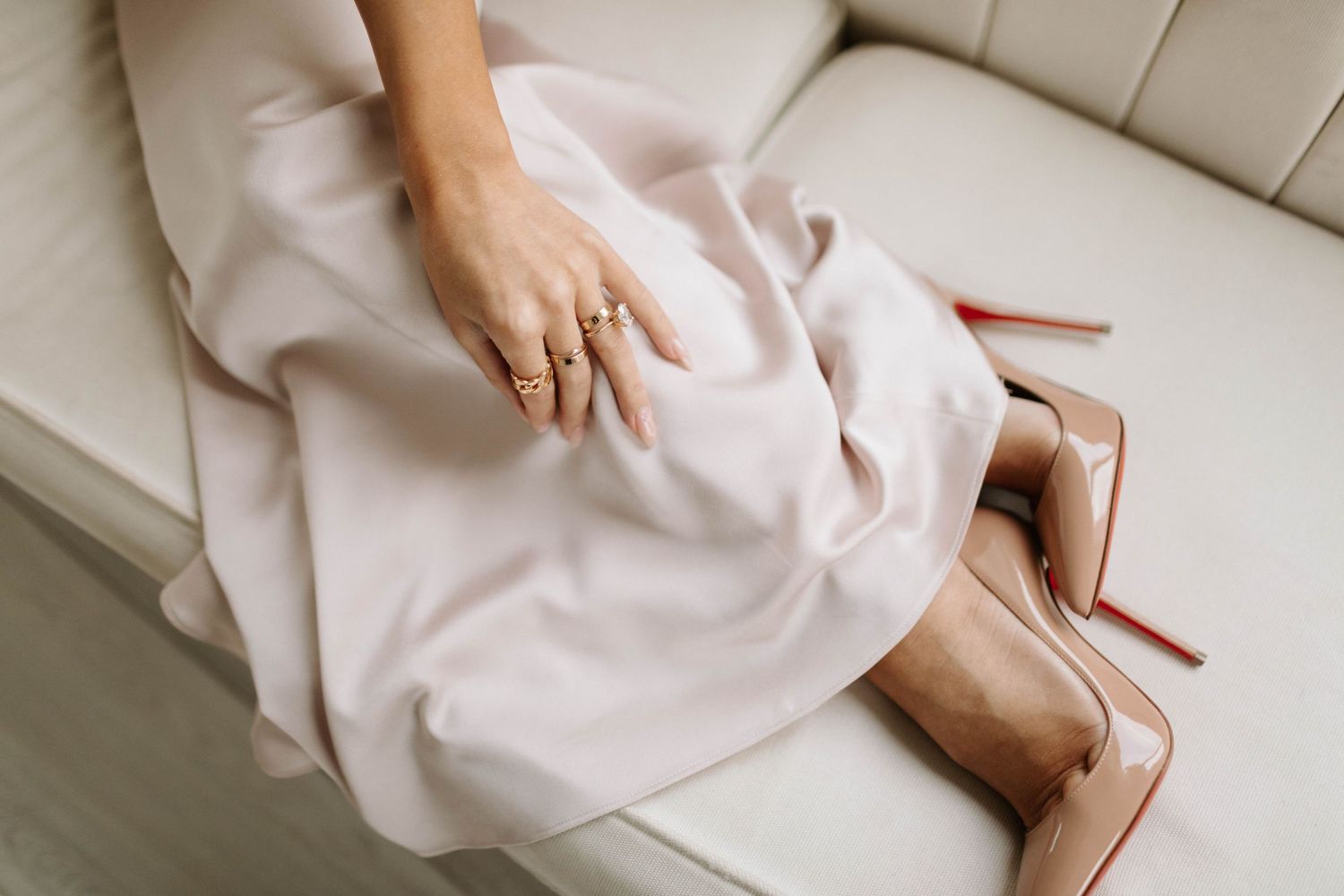 Woman wearing white dress and high heels sitting on a beige couch.