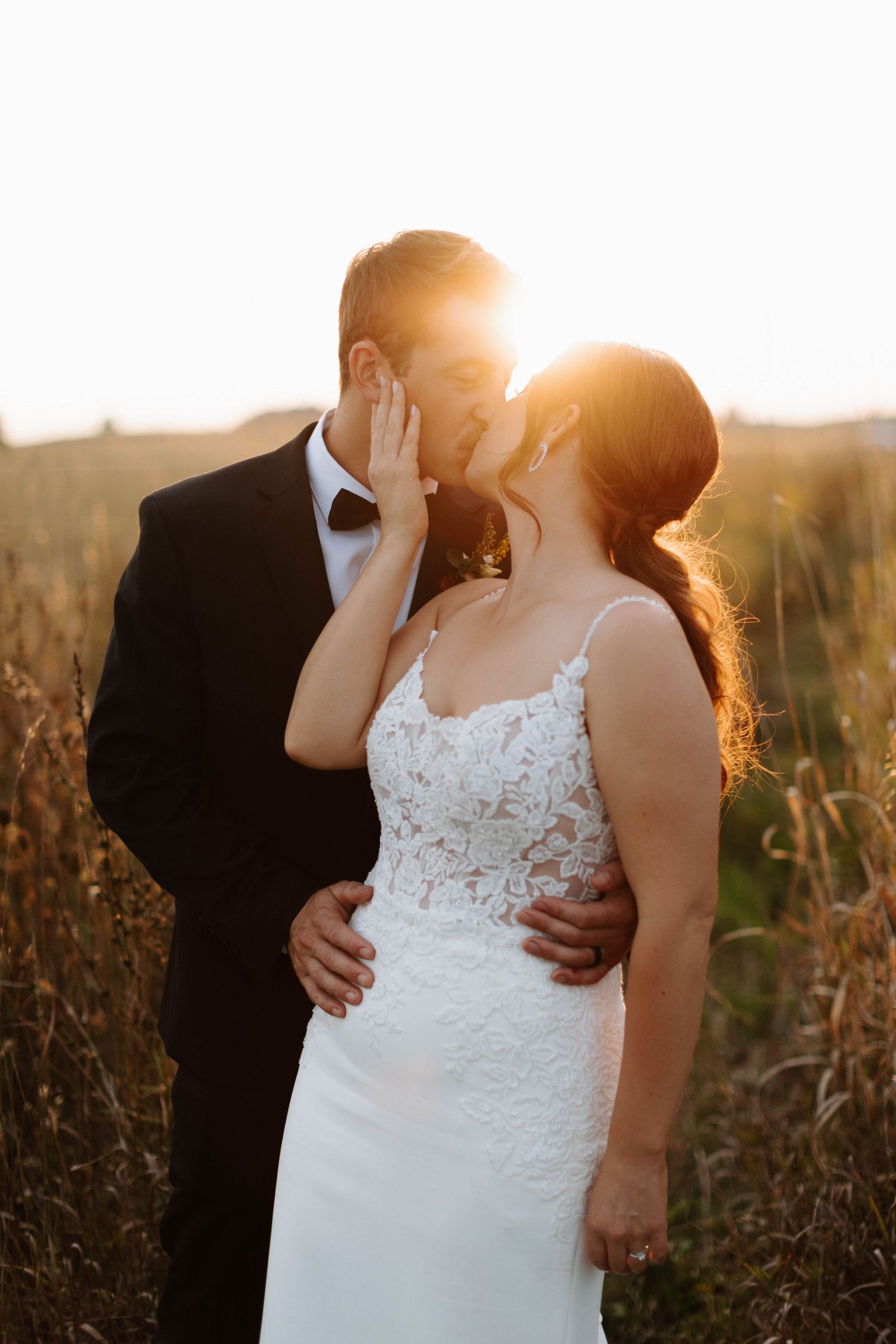 Intimate sunset portrait of bride and groom sharing tender moment in golden field.