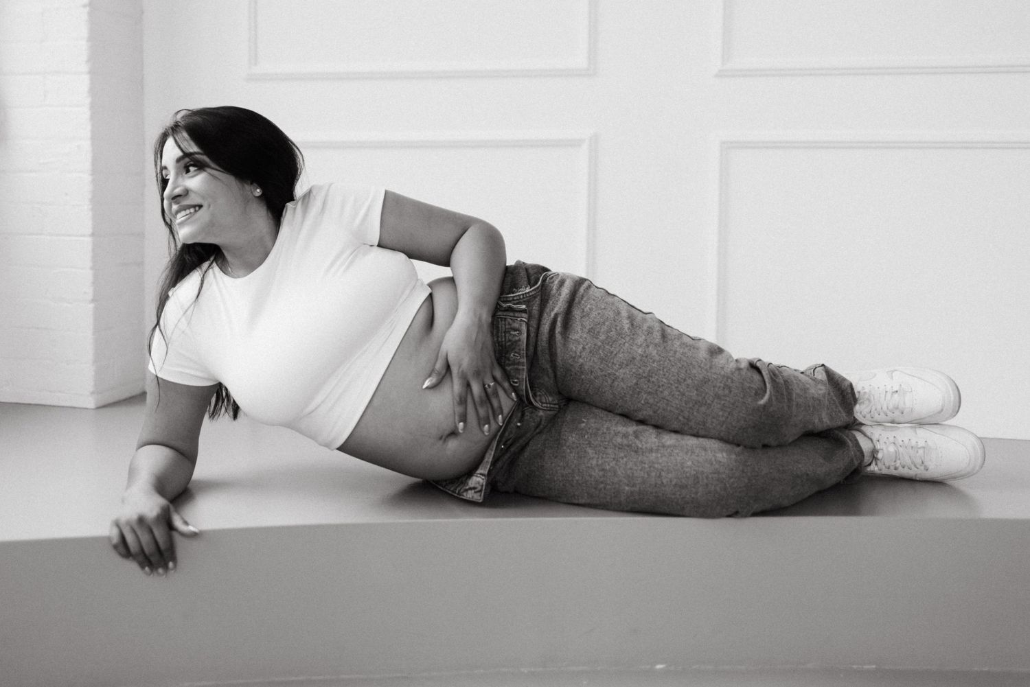 Black and white photo of someone lying down wearing a white crop top and jeans against a light background.