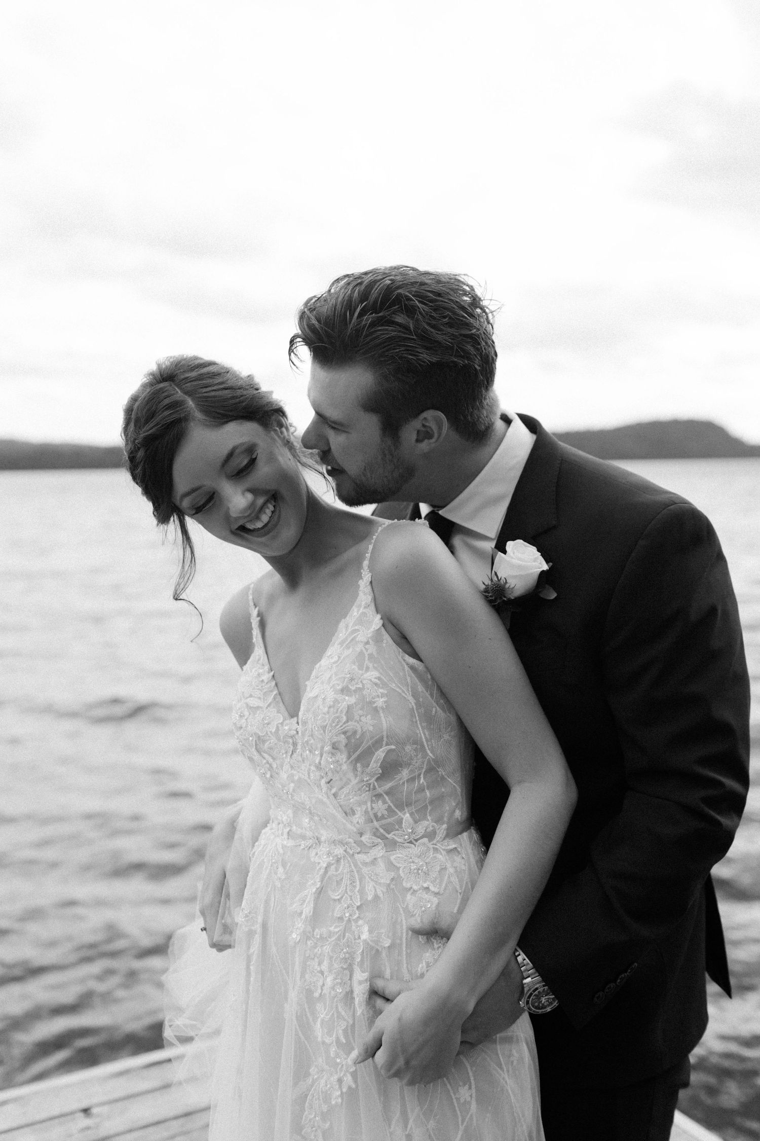 A romantic black and white photo of a couple sharing an intimate moment on a dock by the water.