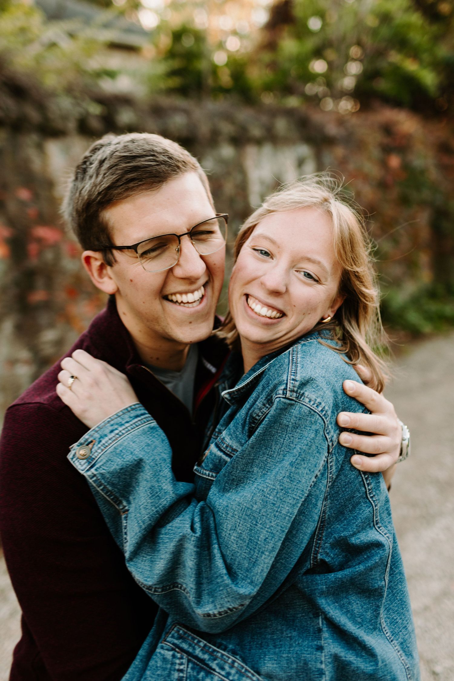A joyful couple laughing and embracing outdoors while wearing a denim jacket and burgundy sweater at the Elora Mill, Ontario.