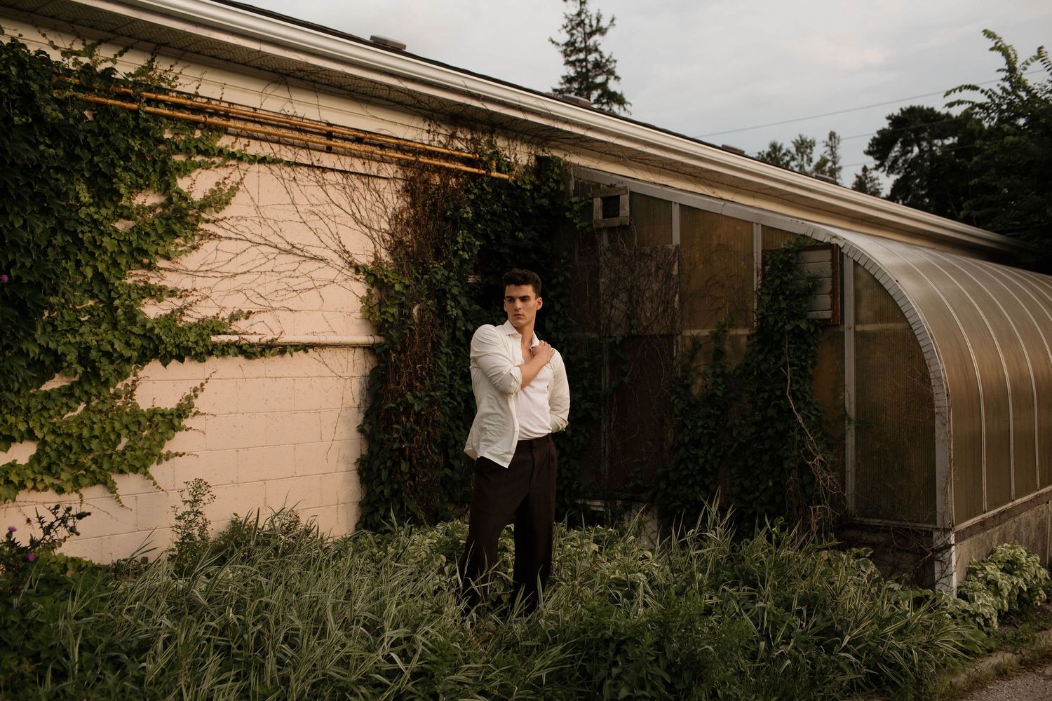 A man in white stands beside a greenhouse wall draped in climbing vines during golden hour lighting in Guelph Ontario