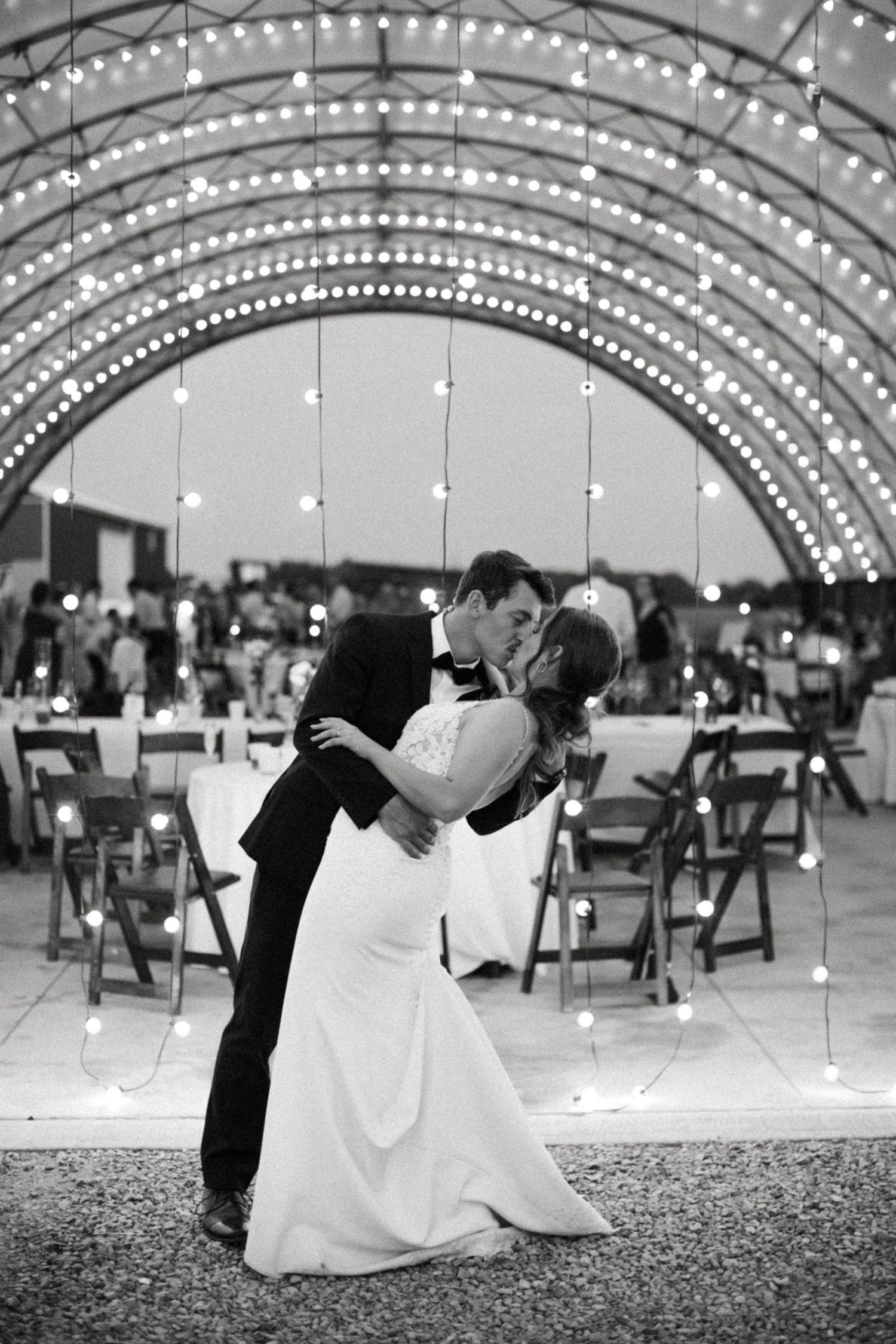 A romantic black and white wedding photo shows a couple dancing under an illuminated arched canopy with string lights in Brantford Ontario