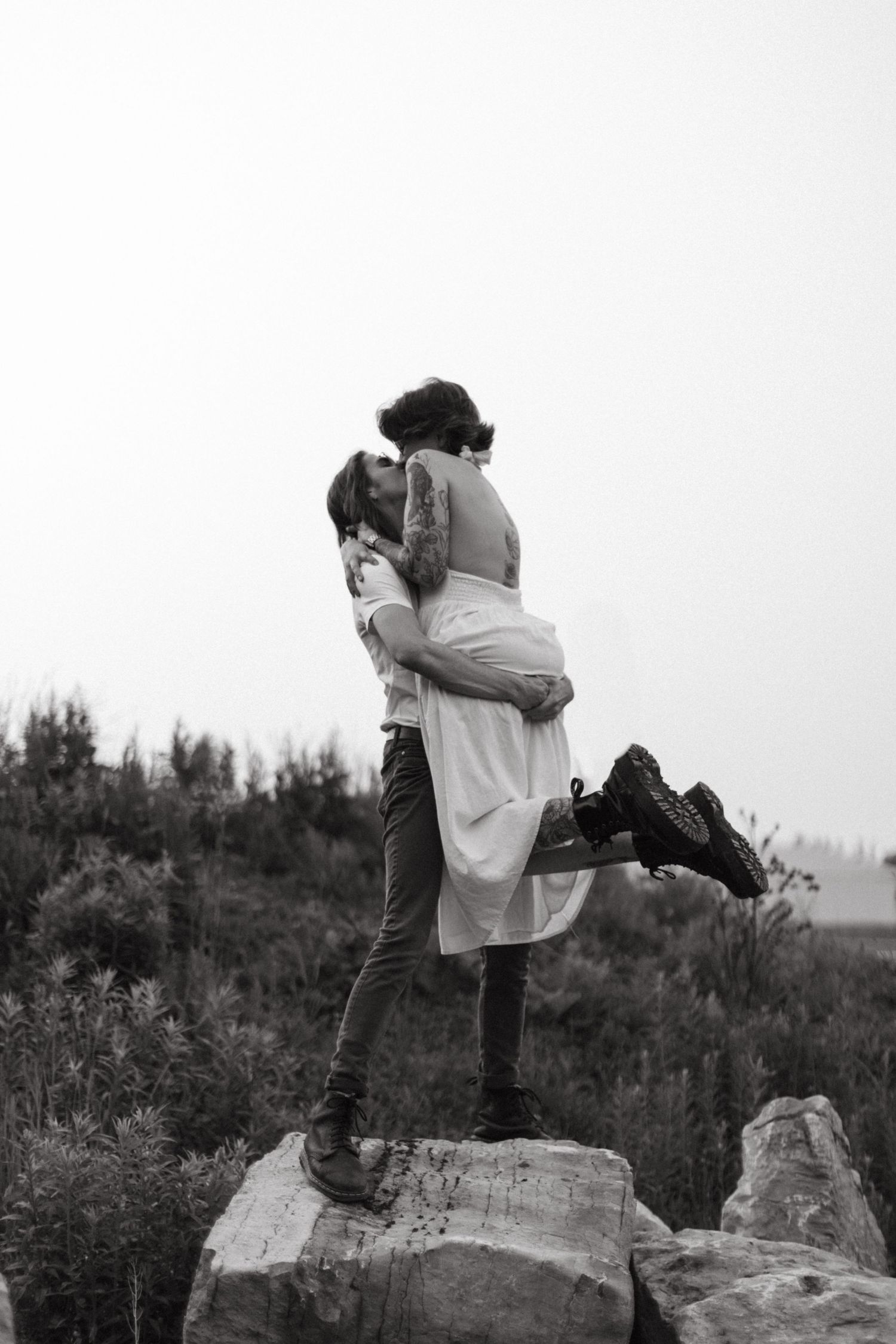 A couple shares a romantic embrace while standing on a rock in black and white photography. Taken in Kitchener Ontario at Bechtel Park.