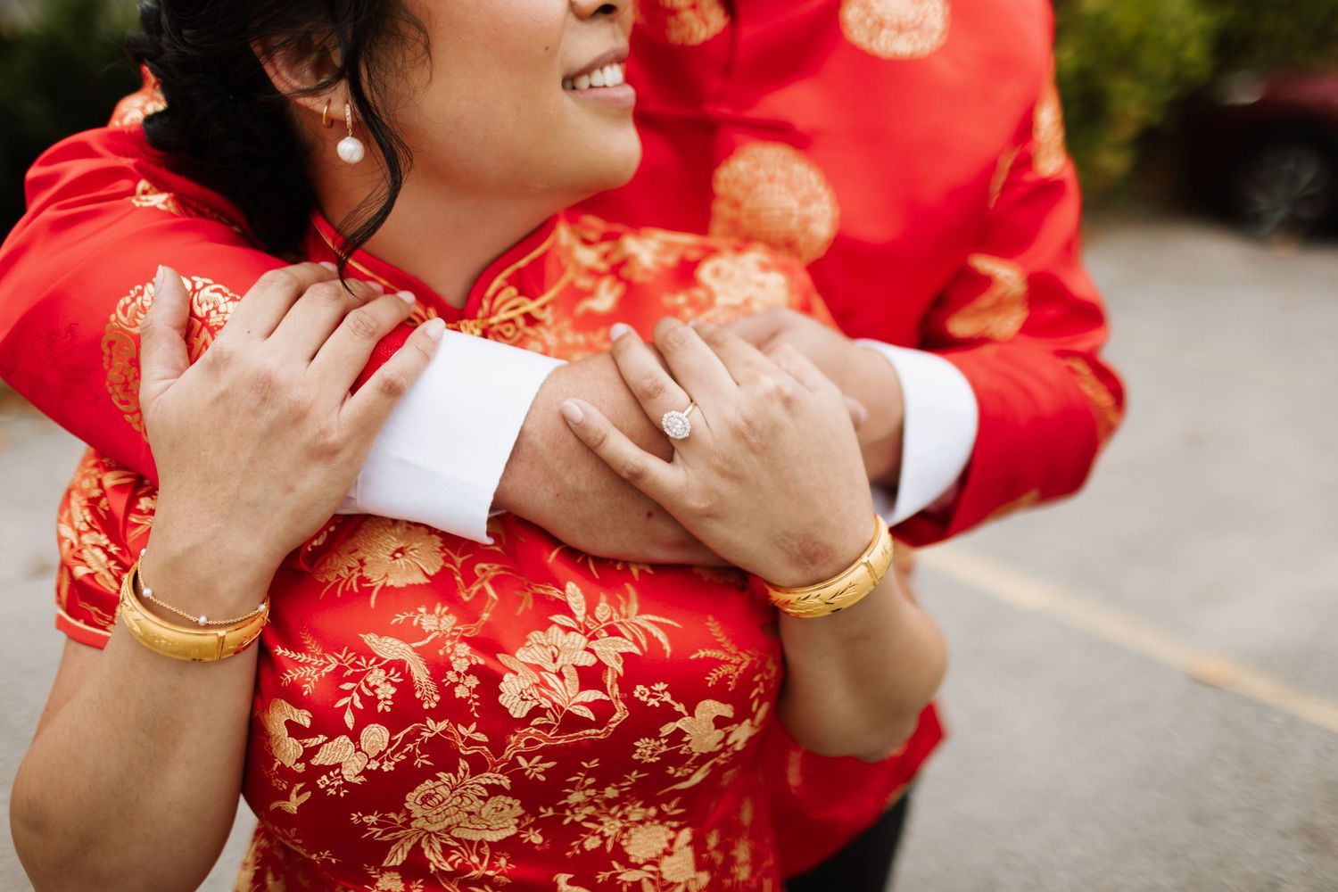 Close-up detail of hands on traditional red Chinese cheongsam dress with gold embroidered pattern and white cuffs.