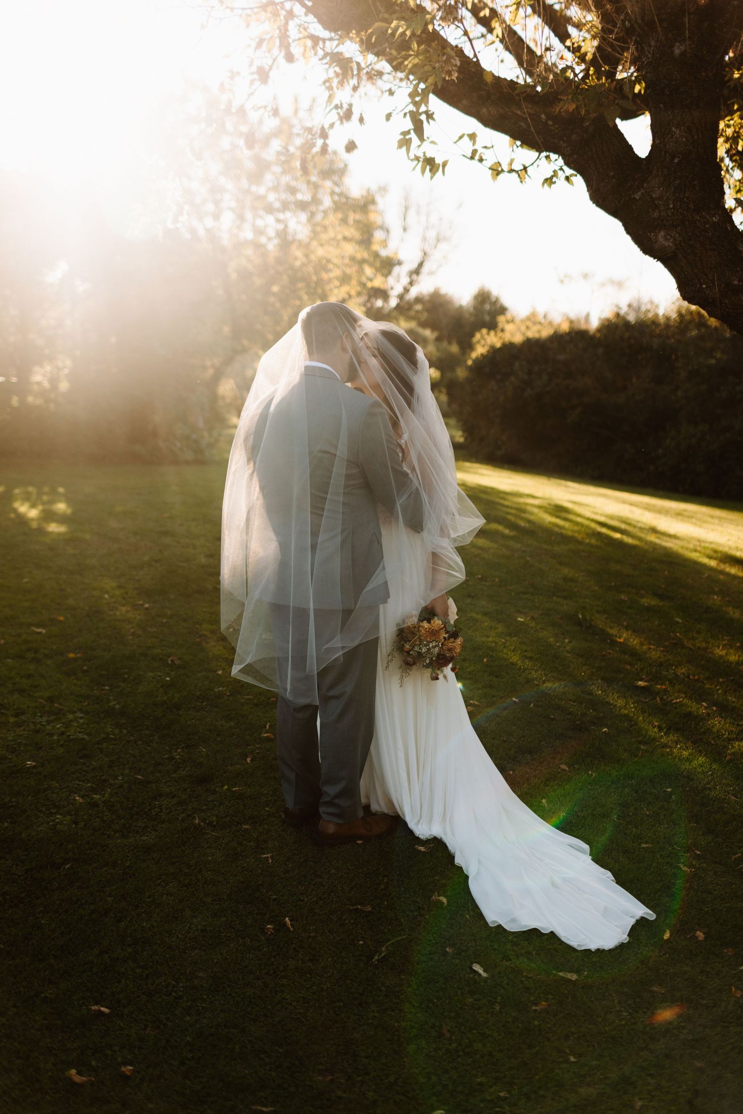 Wedding couple kissing in golden sunset light under a tree with flowing white dress and veil creating romantic silhouette in Guelph Ontario