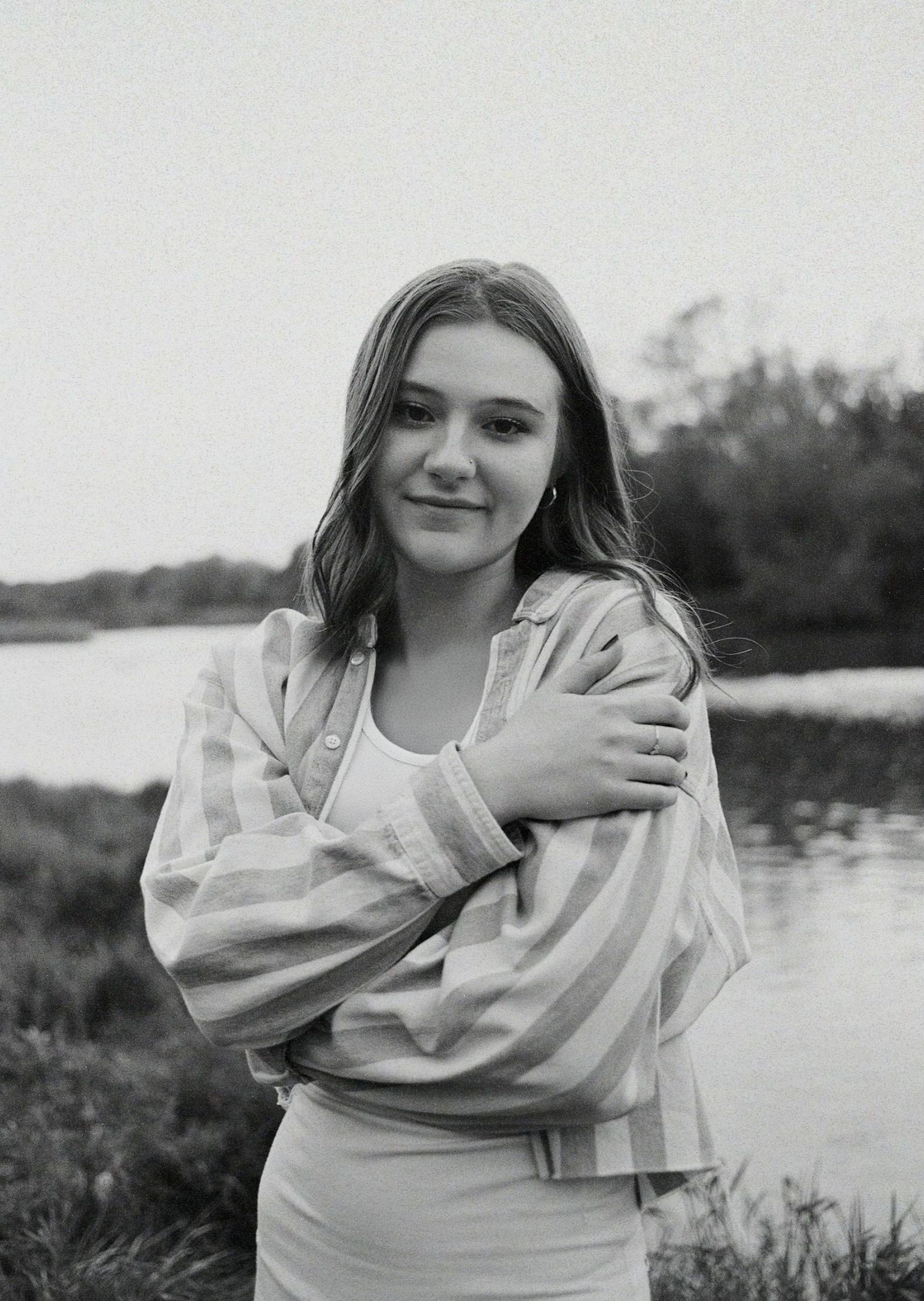 Black and white portrait series of someone in a light colored dress posing by a lake during a photoshoot.